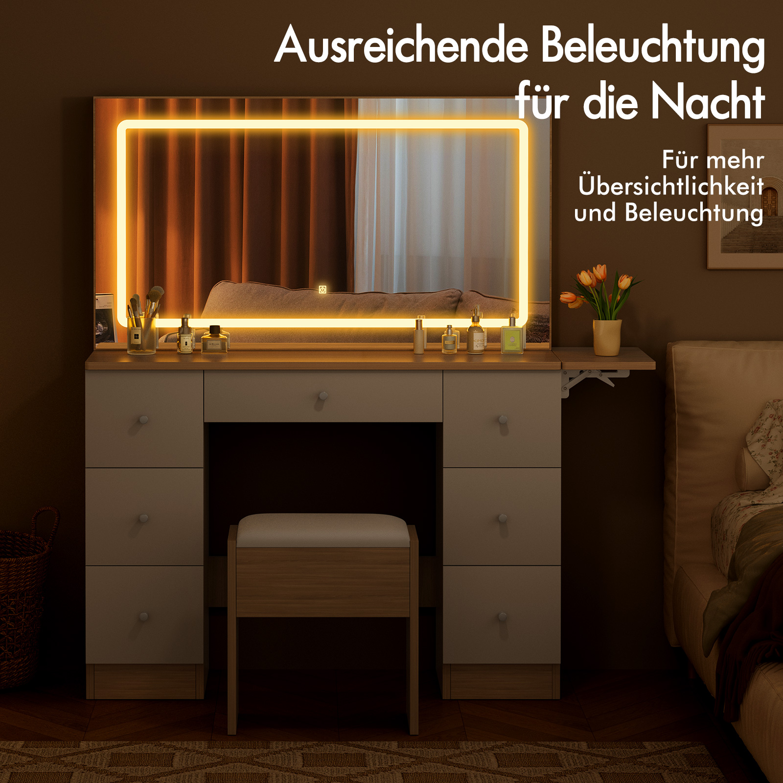 Ein Schminktisch mit beleuchtetem Spiegel, Kosmetik und Blumen. Daneben ein Bett.