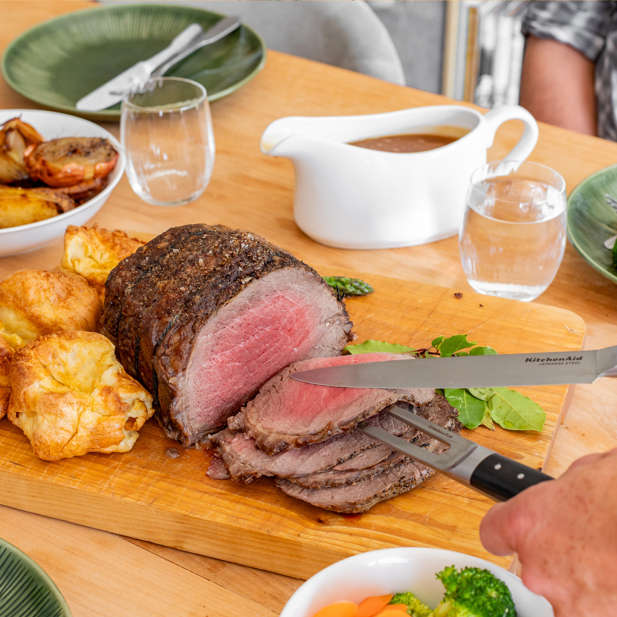 Ein Braten wird auf einem Holzbrett angeschnitten, serviert mit Yorkshire Pudding.