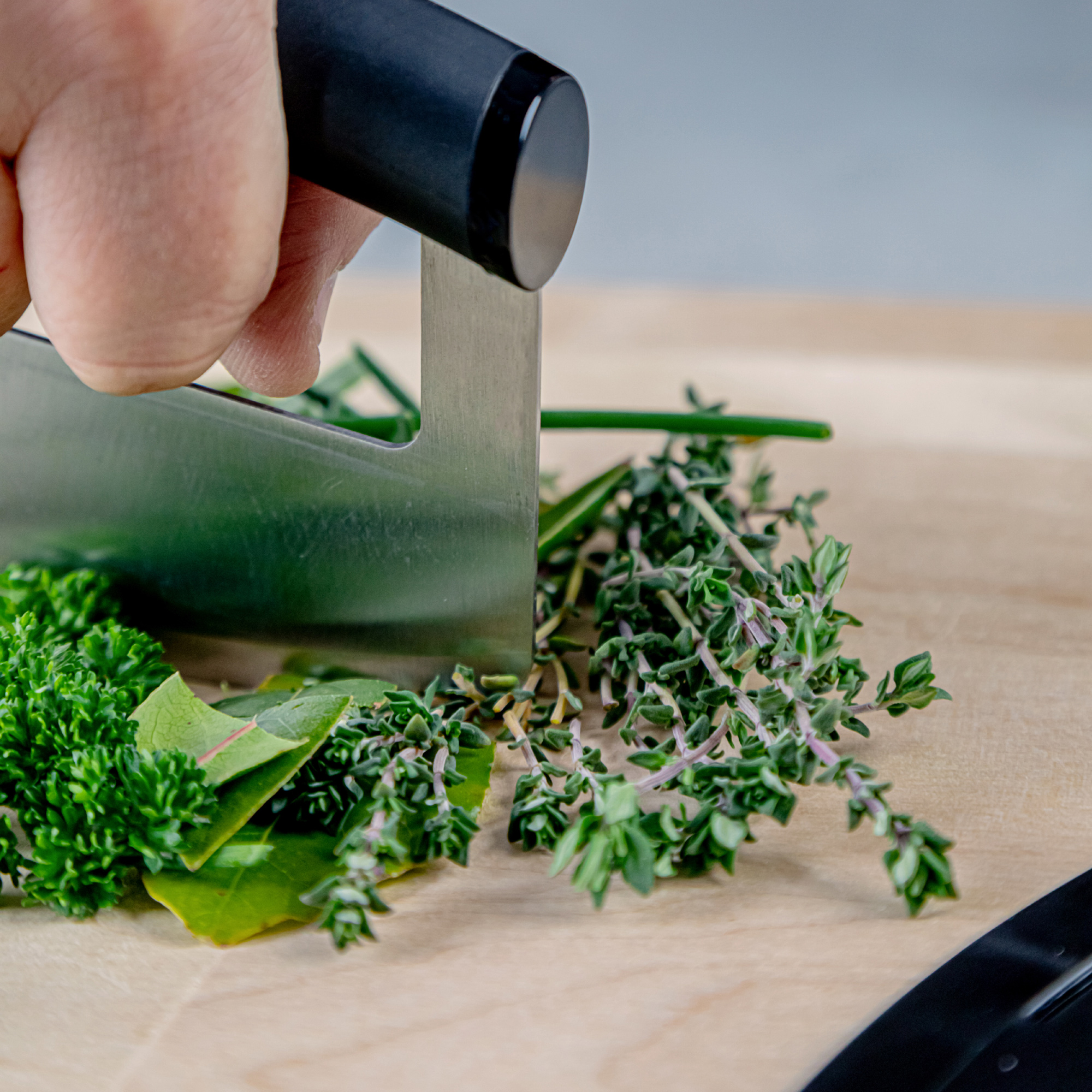 Eine Hand hackt frische Kräuter wie Petersilie und Thymian auf einem Holzbrett.