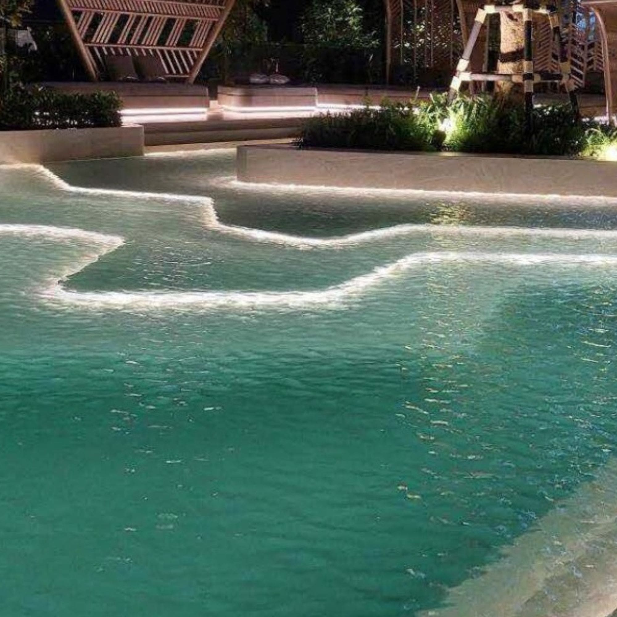 Una piscina moderna con niveles escalonados y suave iluminación blanca por la noche.