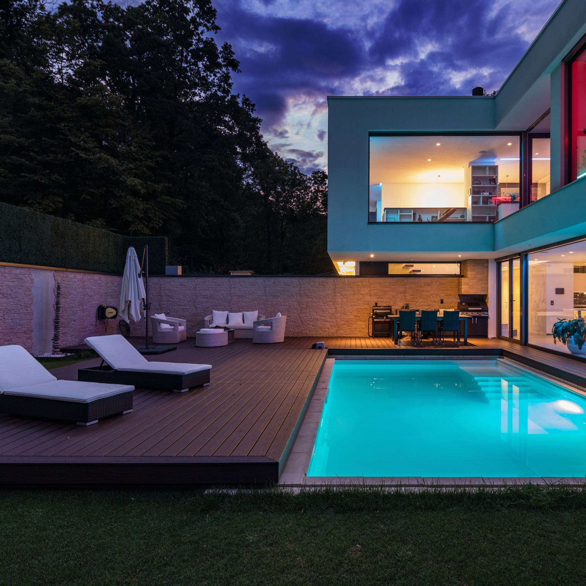 Villa moderna con piscina de noche, iluminada con luz azul.