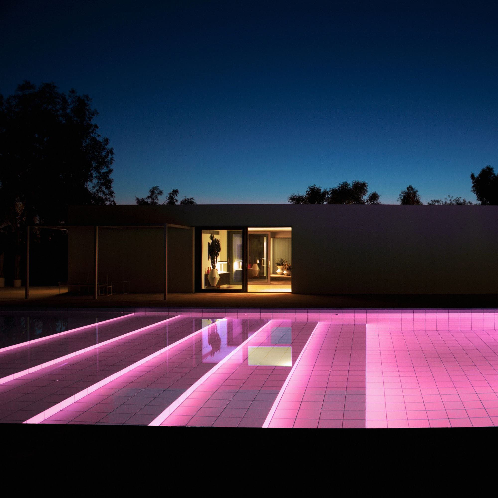Una casa moderna con piscina por la noche. Luces rosas iluminan los escalones de la piscina.