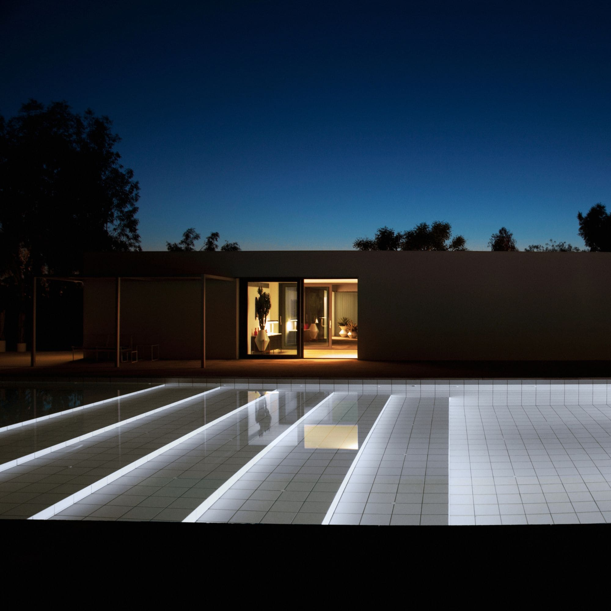 Villa moderna de noche con piscina iluminada y cielo nocturno.