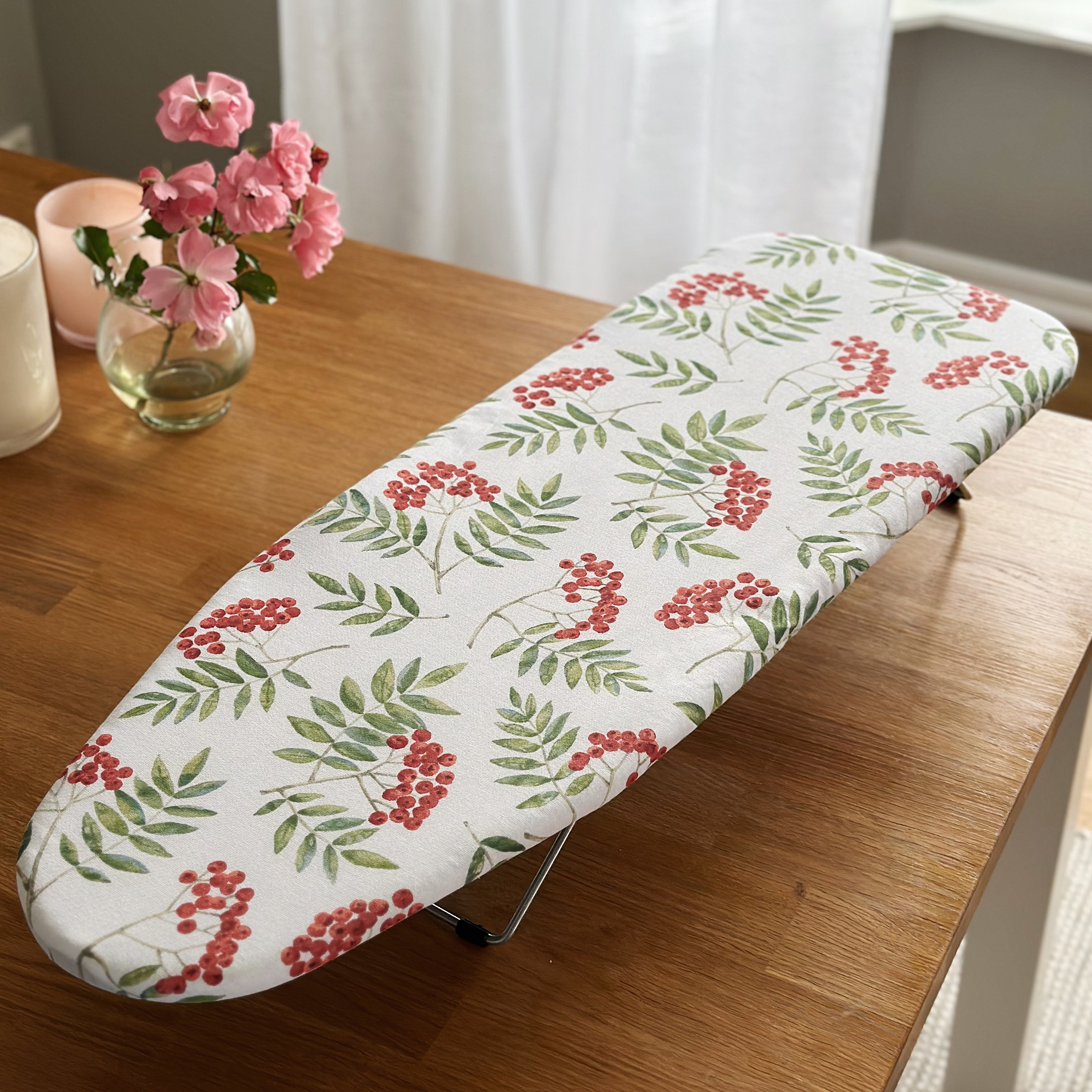 Planche à repasser avec baies rouges et feuilles vertes sur tissu blanc sur table en bois.