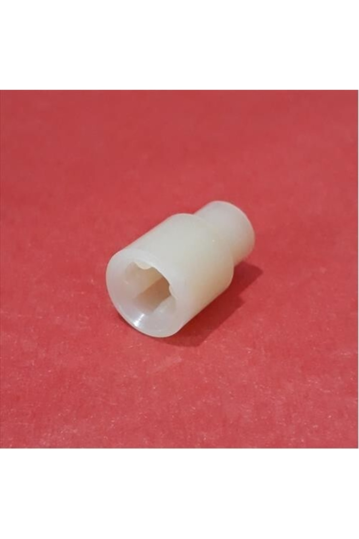 Altıgen delikli beyaz plastik adaptör kırmızı zemin üzerinde duruyor.
