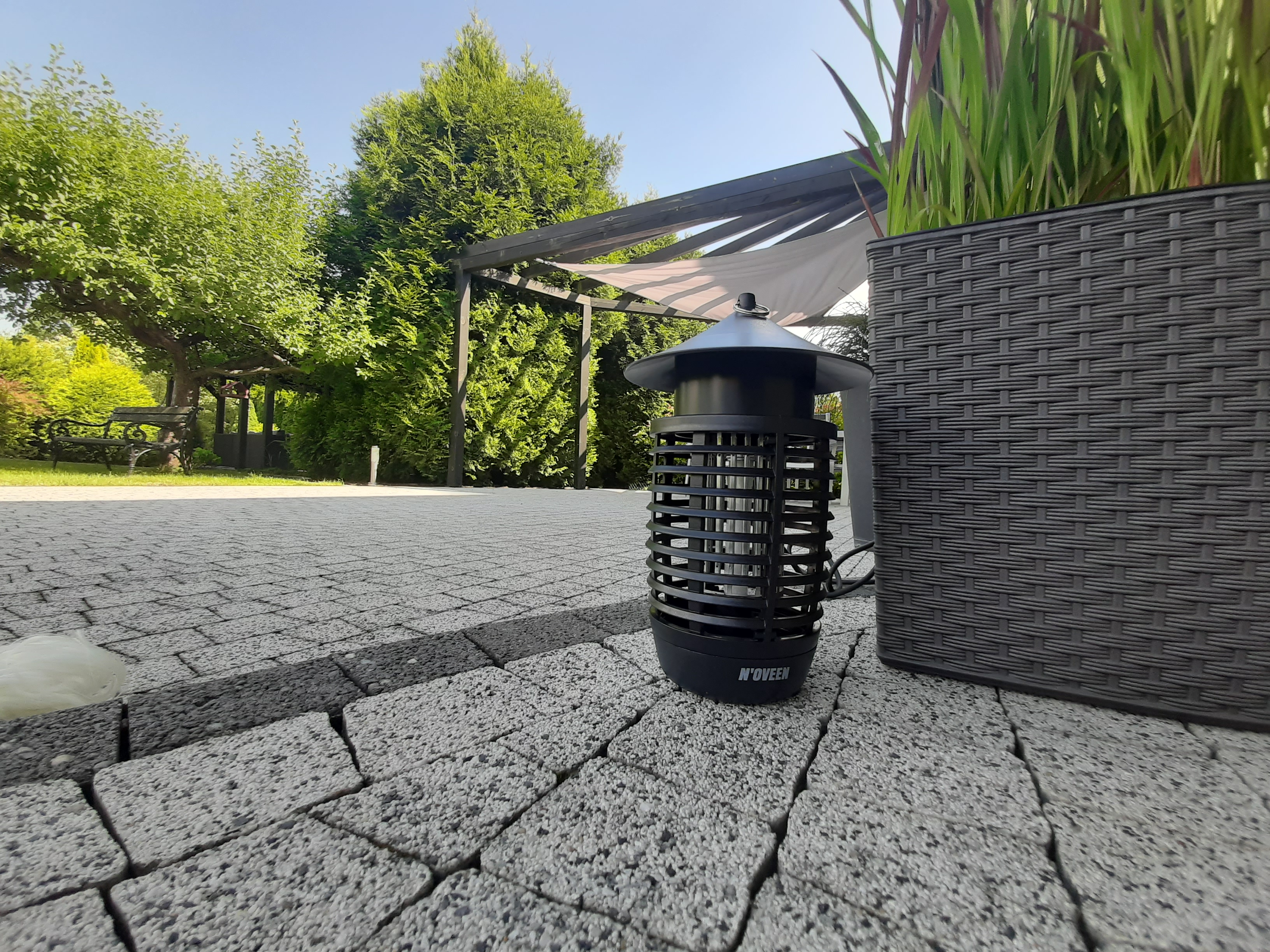 Czarna lampa owadob0jcza stoi na wybrukowanym patio obok plecionego kosza.
