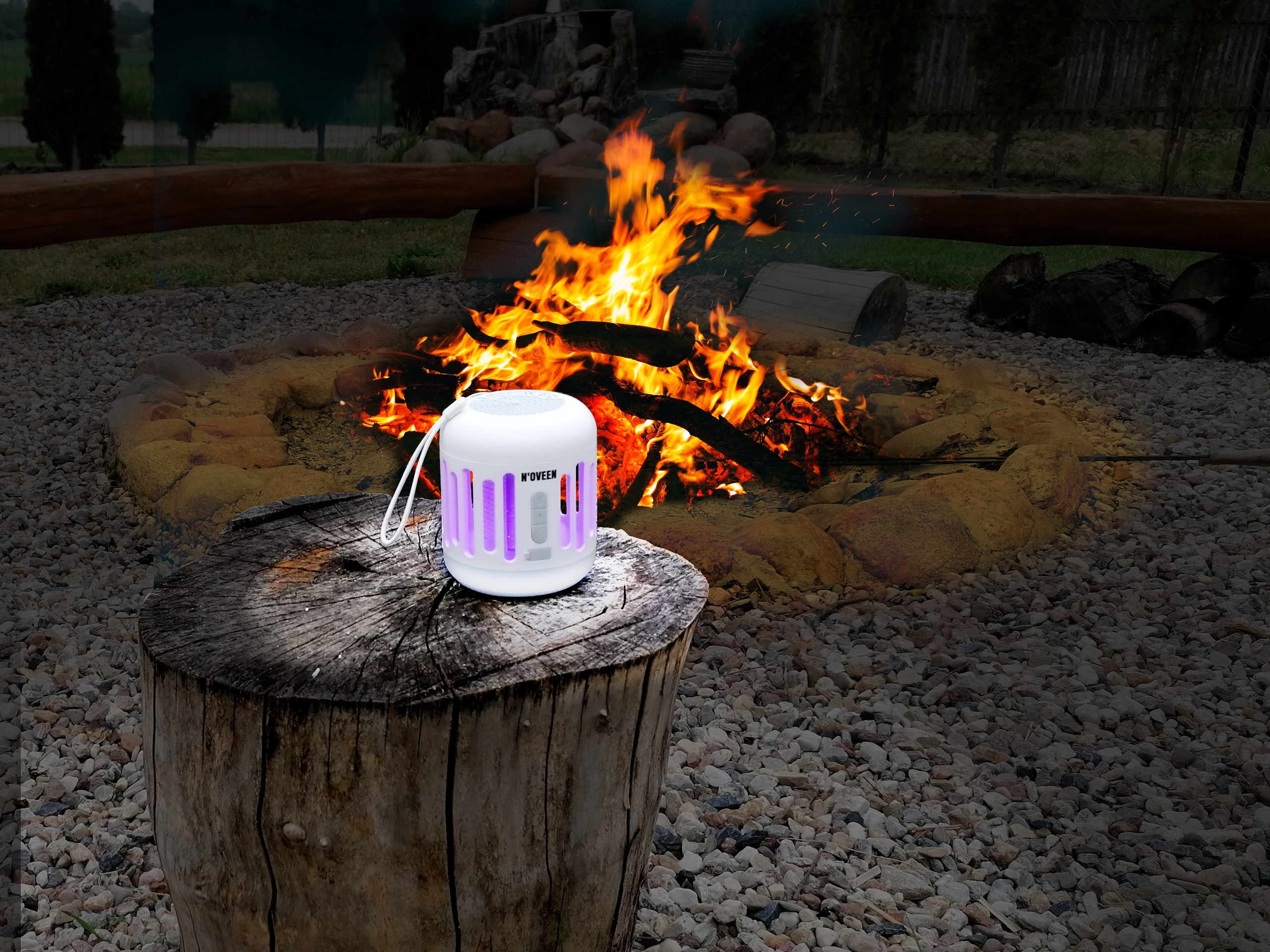 Biały głośnik z fioletowym światłem na pniu drzewa przy ognisku.