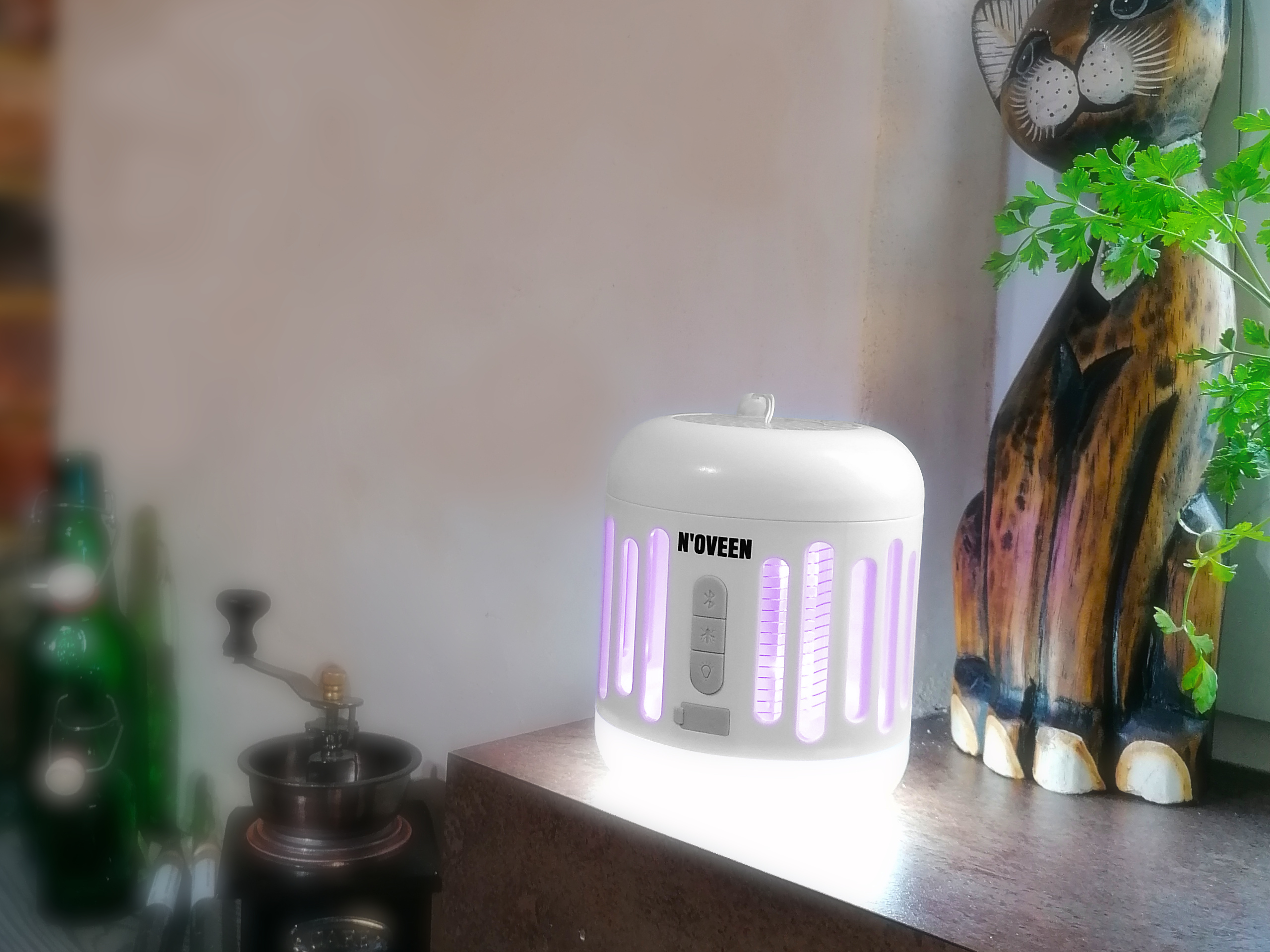 Biała lampa owadobójcza N'oveen z fioletowym światłem stoi obok drewnianego kota.