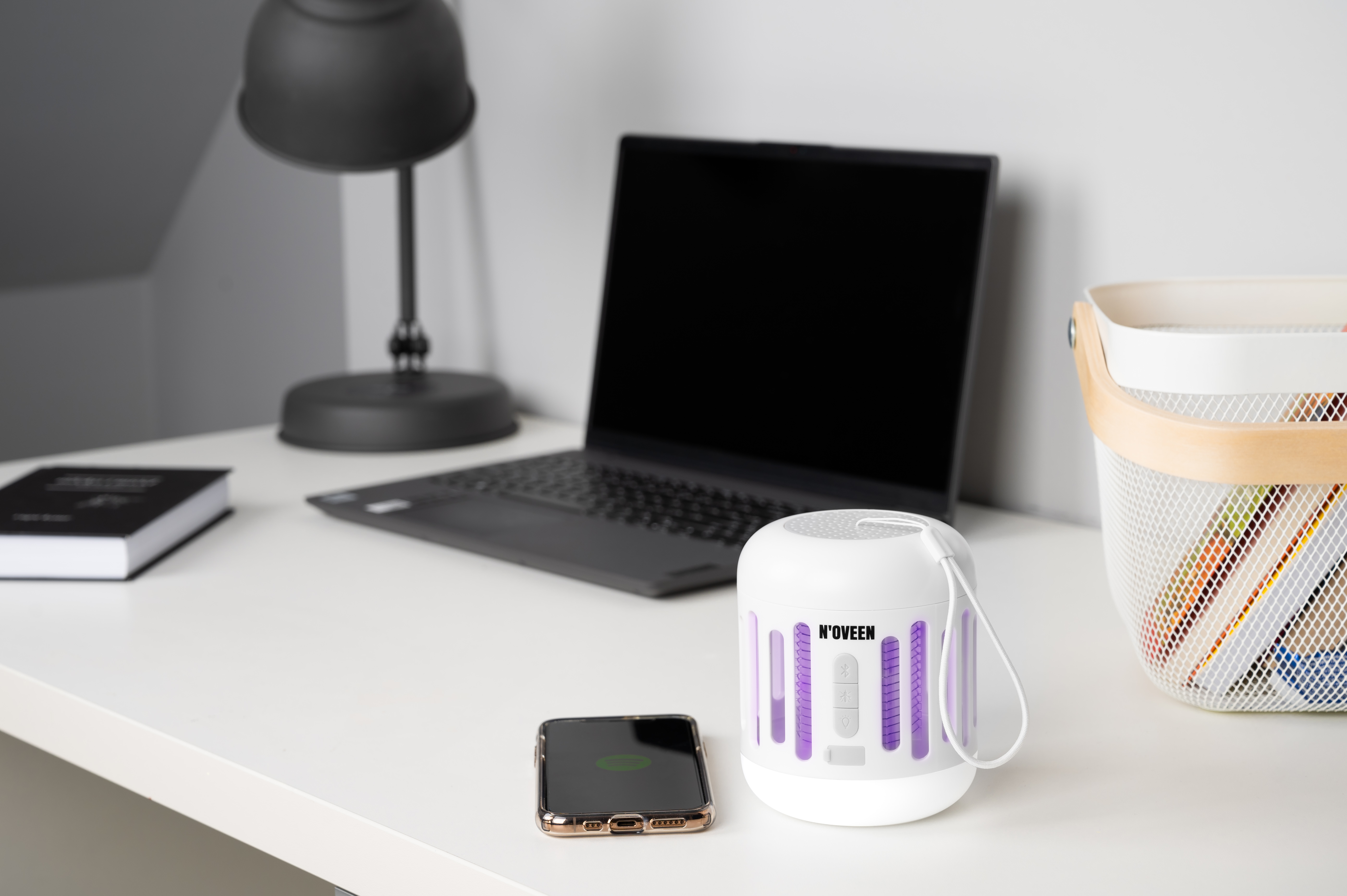 Biała lampa owadobójcza z fioletowymi światłami na biurku obok telefonu.