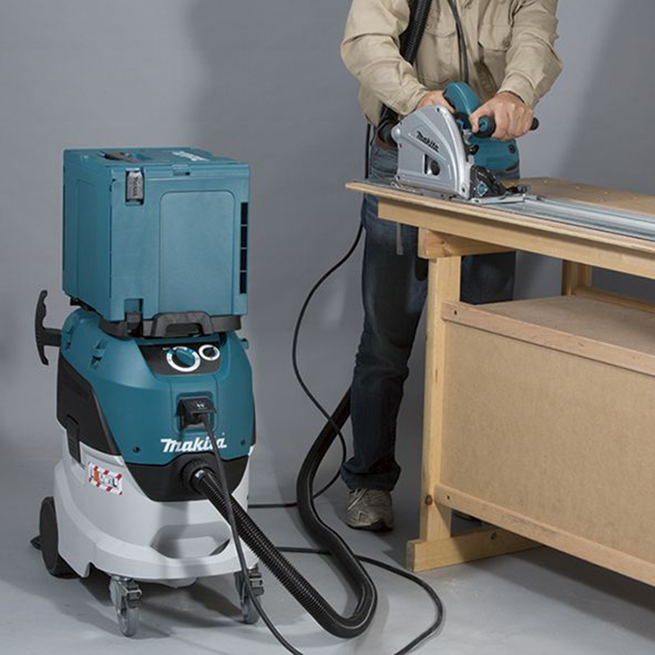 Mężczyzna tnie drewno piłą tarczową, obok stoi niebieski odkurzacz.
