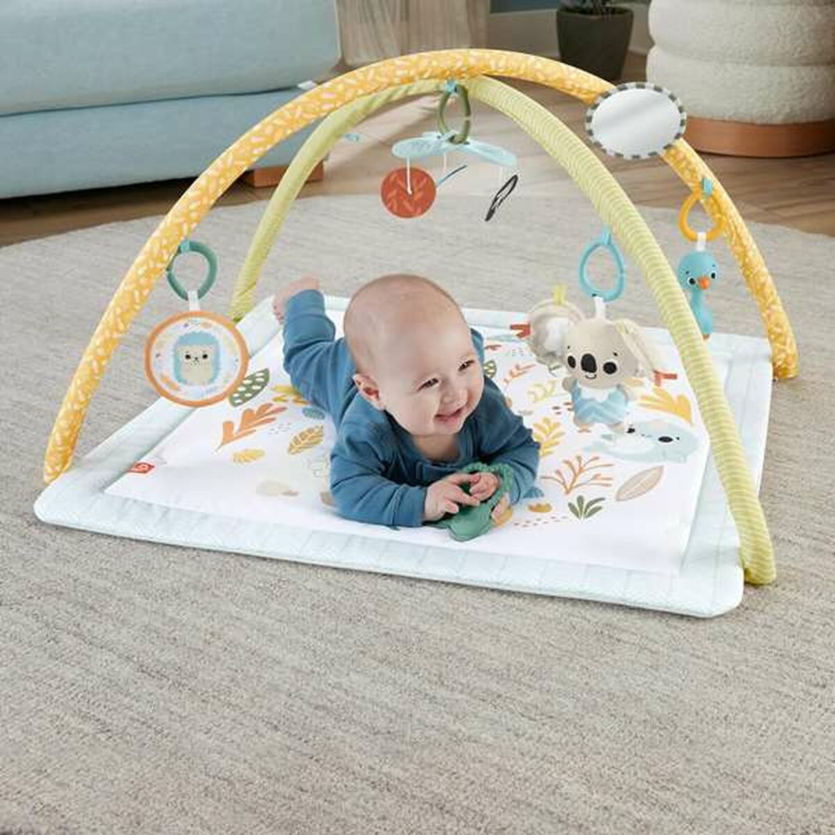 Ein Baby liegt auf einer Spielmatte unter einem Spielbogen mit Spielzeug.