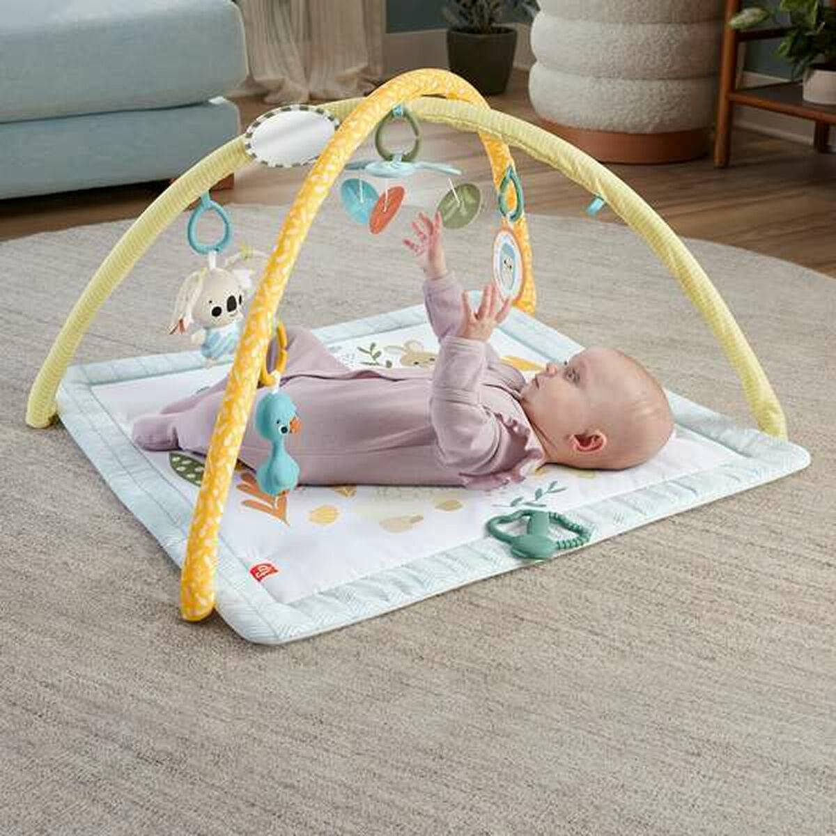 Baby liegt auf einer Spielmatte mit Spielzeug, das an einem gelben Bogen hängt.