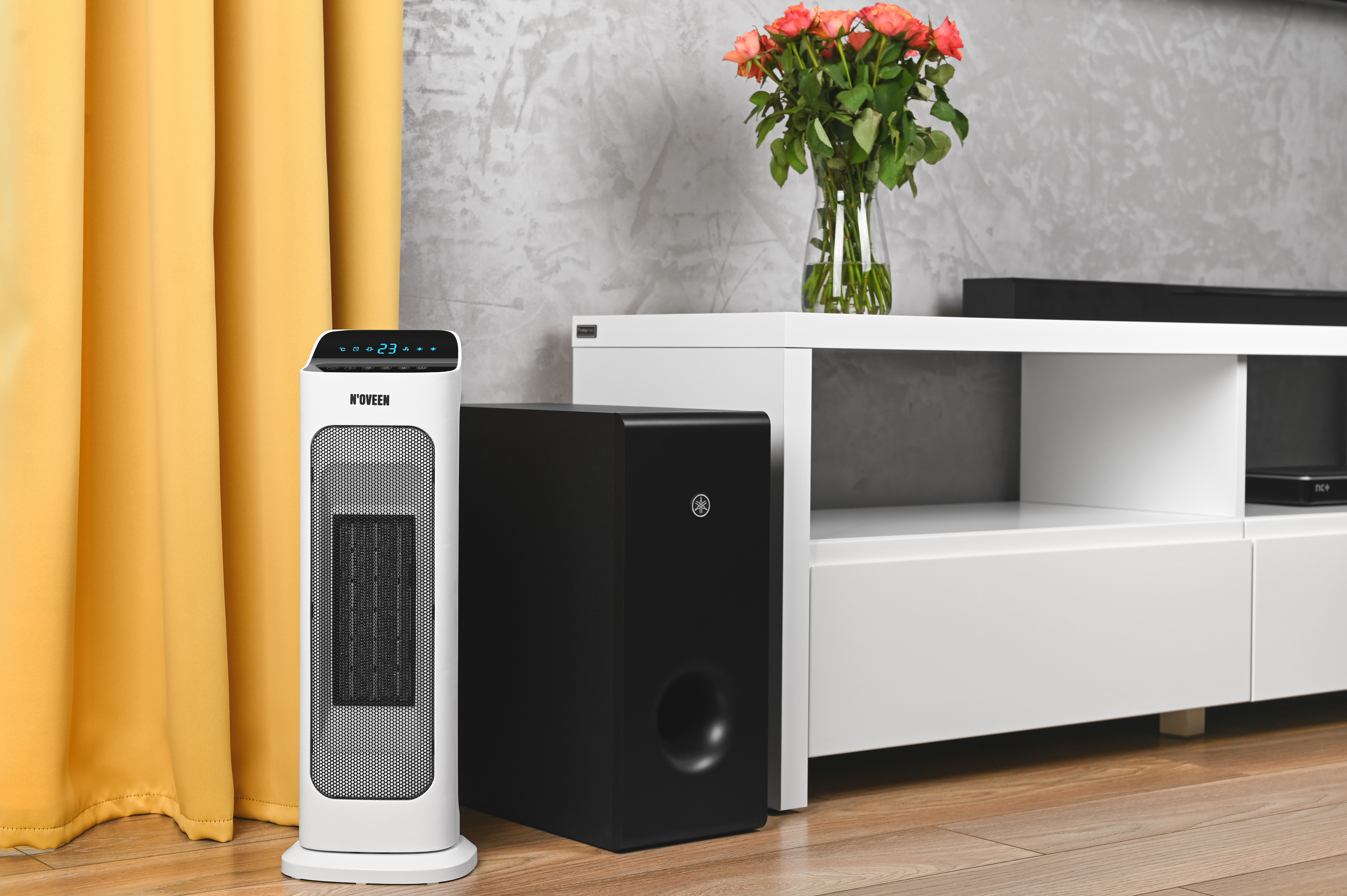 Biały grzejnik stoi obok żółtych zasłon i czarnego subwoofera.