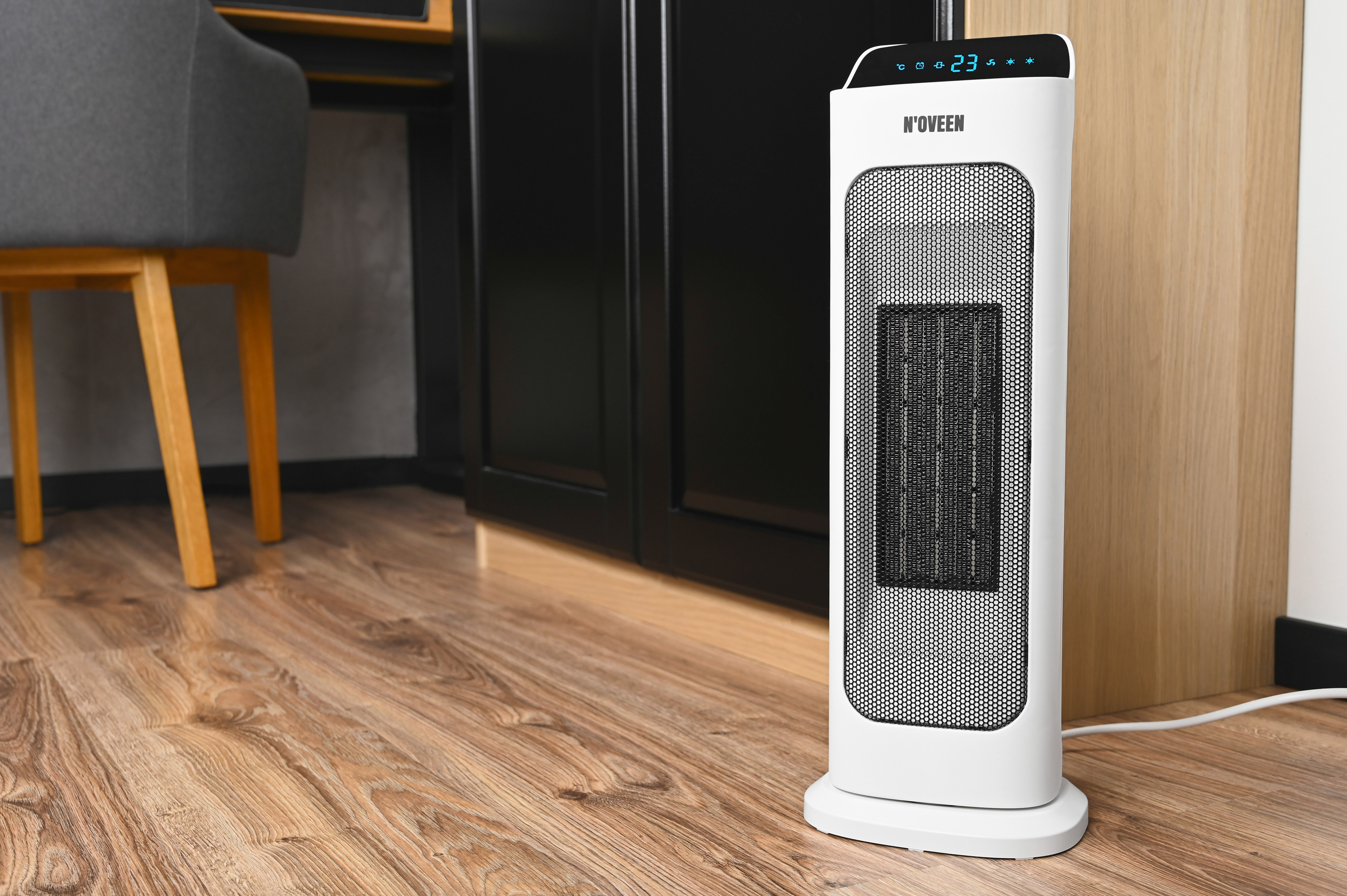 Biały grzejnik wieżowy z czarną kratką stoi na drewnianej podłodze.