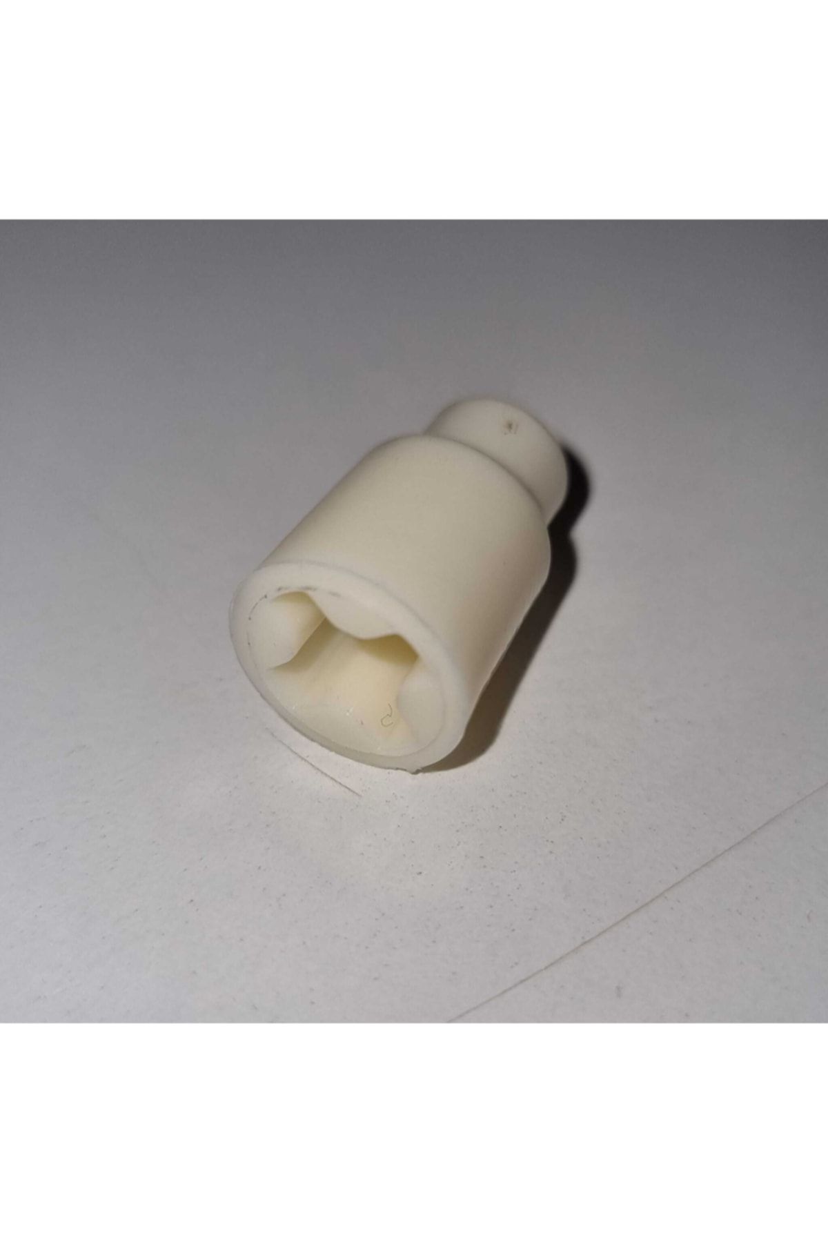 Altıgen açıklıklı beyaz plastik adaptör, dokulu bir yüzeyde duruyor.
