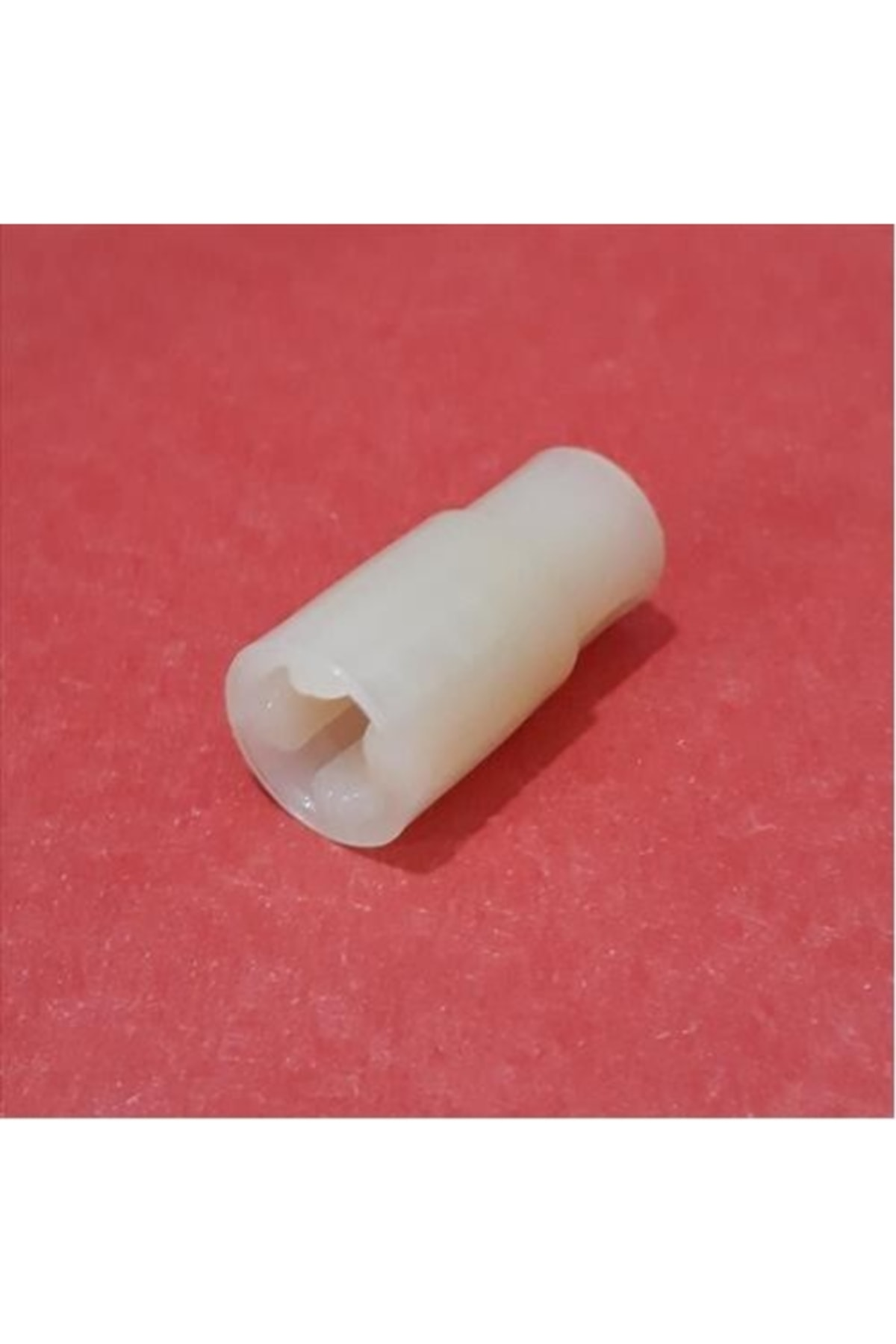 Altıgen uçlu beyaz plastik adaptör kırmızı kumaş üzerinde duruyor.