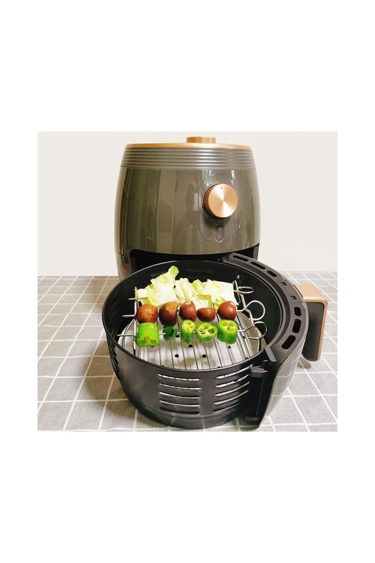 Kareli masa üzerinde, sepetinde sebzeli şişler bulunan bir airfryer.