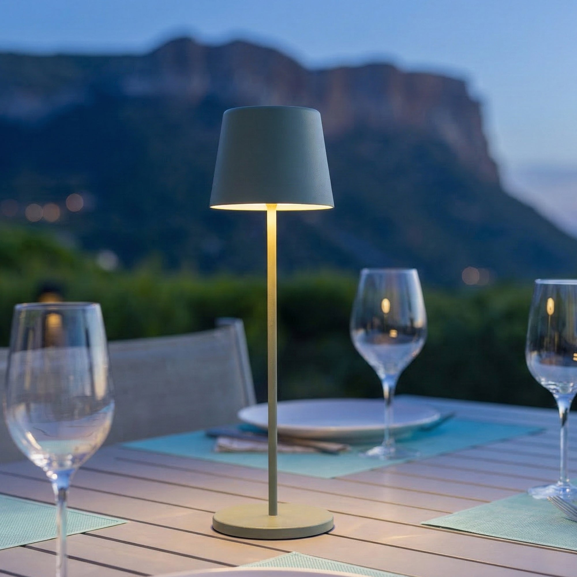 Eine Tischlampe beleuchtet einen Tisch mit Gläsern und Bergen im Hintergrund.