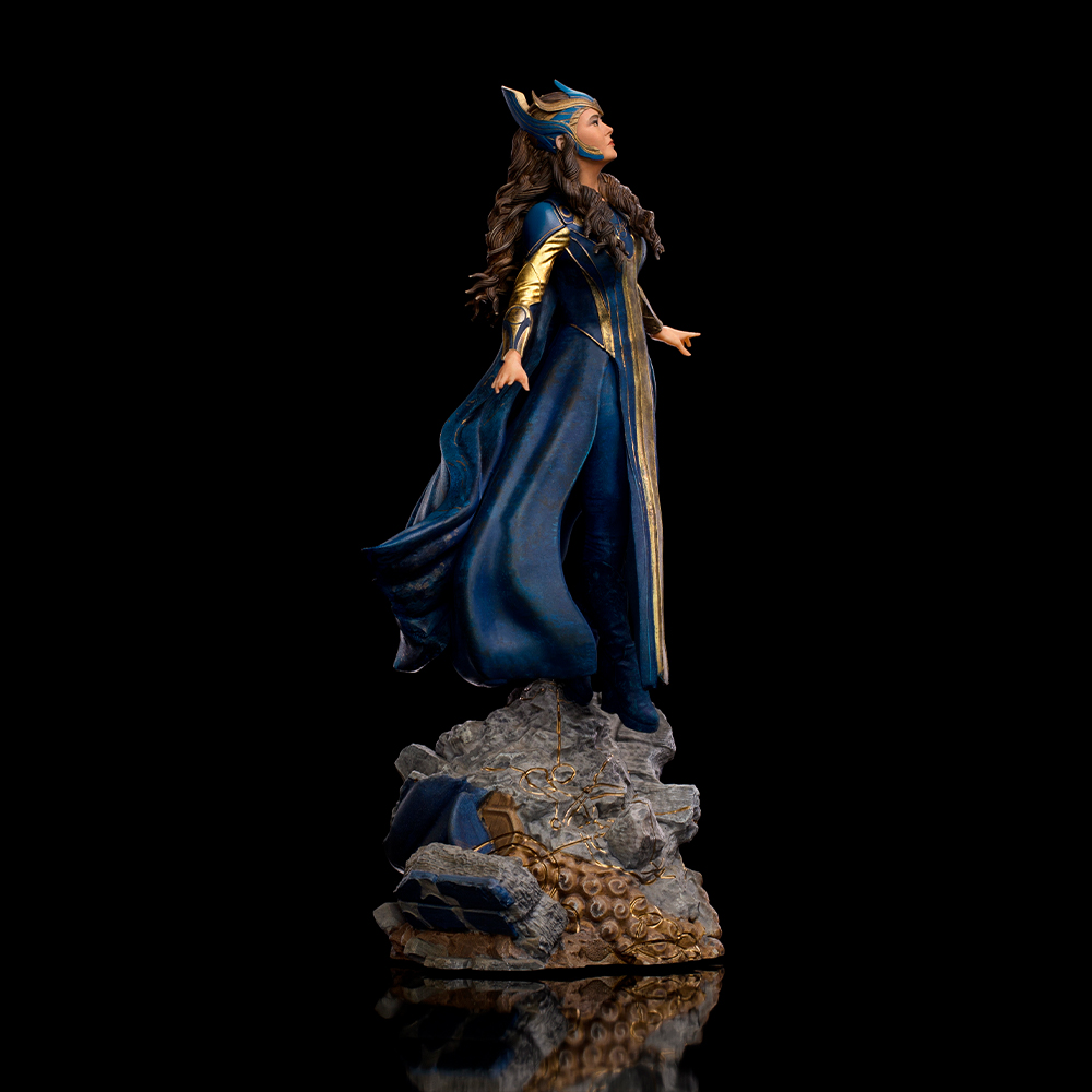 Figura di donna in abito blu con accenti dorati, in piedi su rocce.