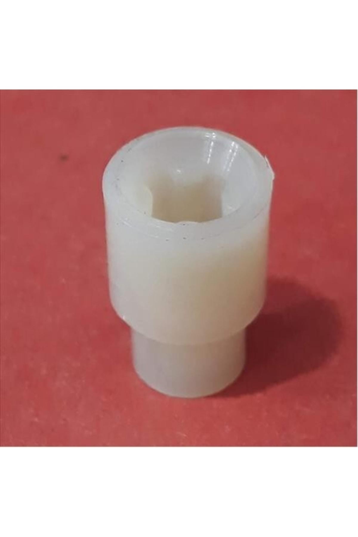 Altıgen delikli beyaz plastik ara parça, kırmızı arka plan üzerinde.