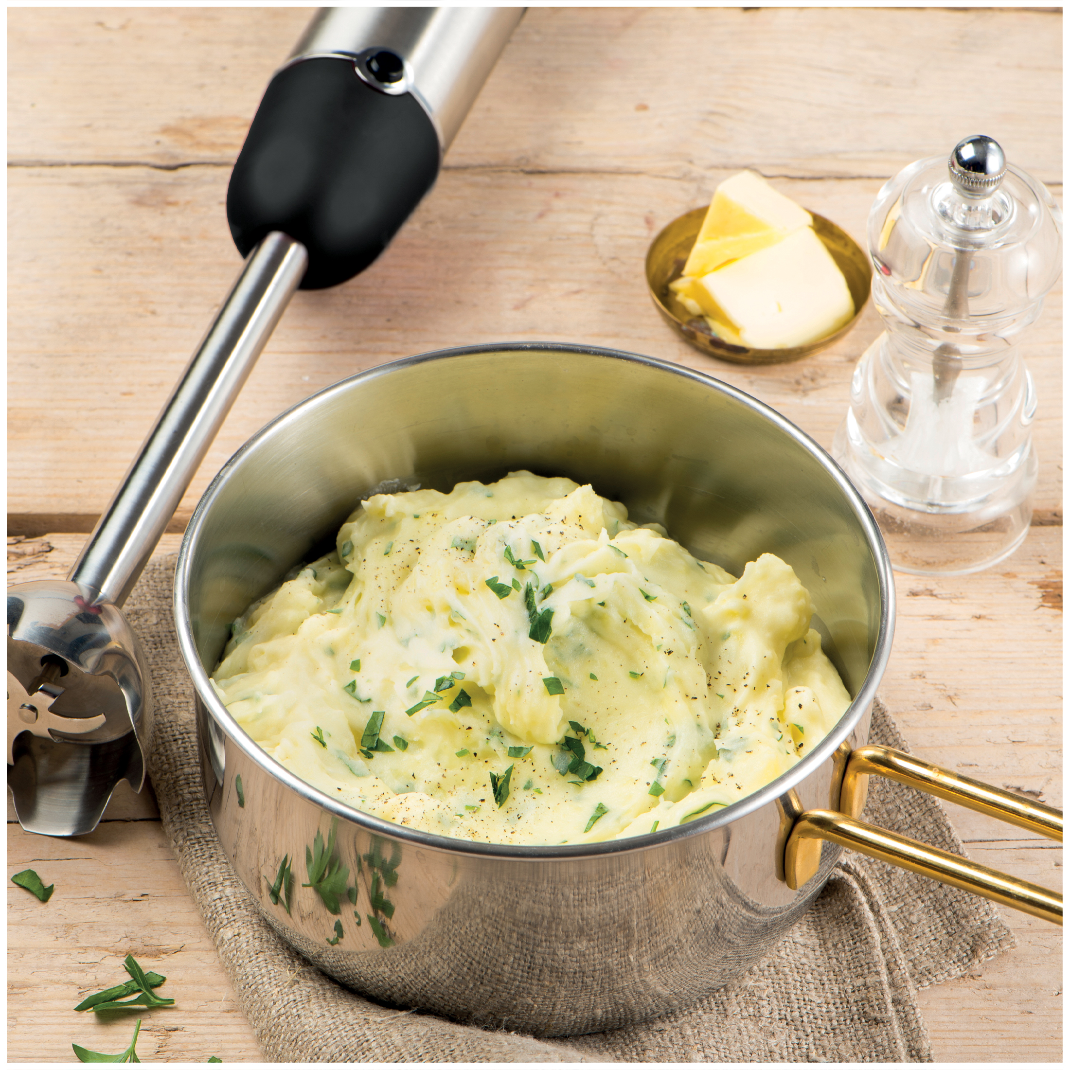 Aardappelpuree met kruiden in een pan, met boter, zoutmolen en staafmixer.