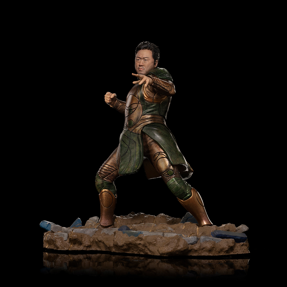 Una figura in armatura verde e oro si erge su una base rocciosa.