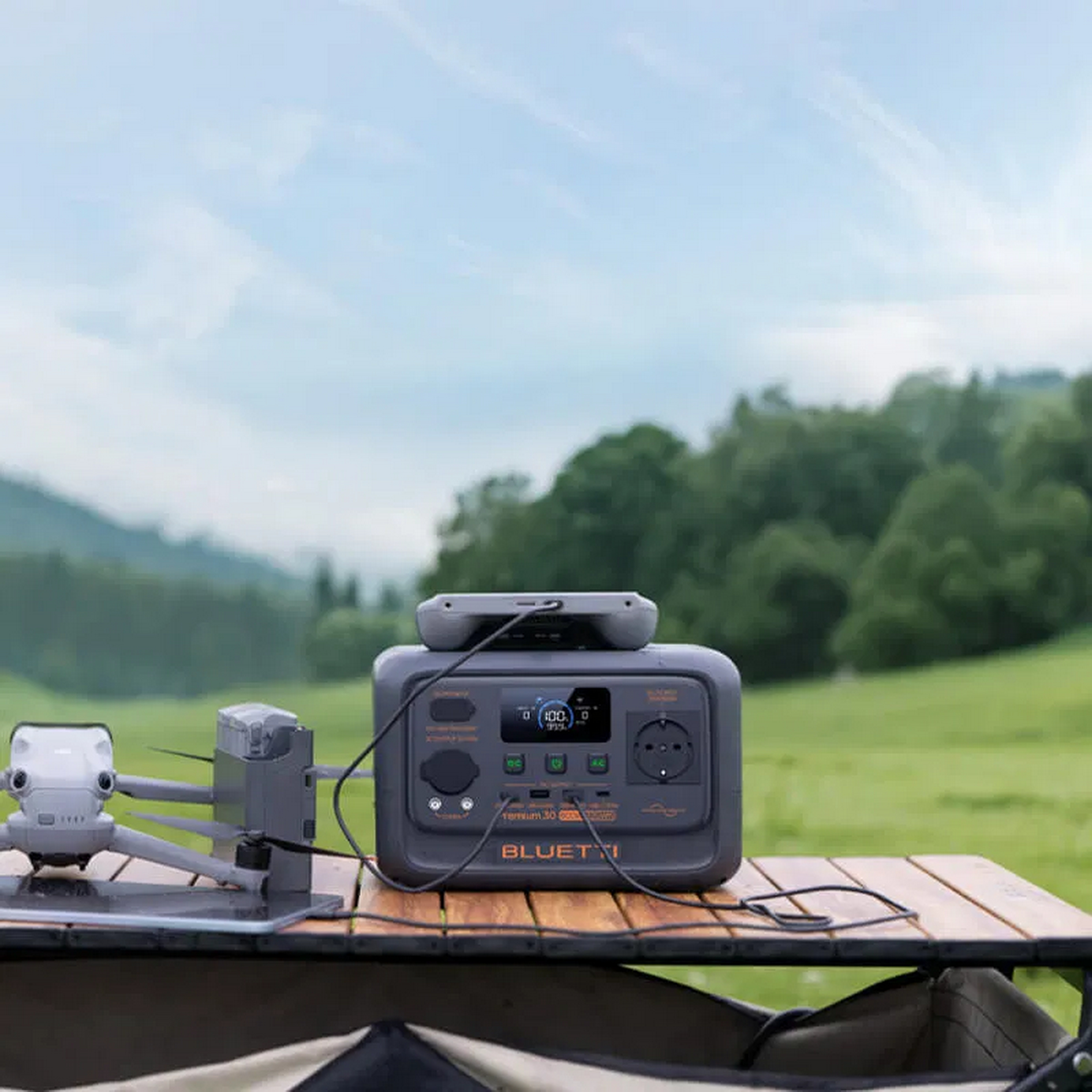 Szara stacja zasilania Bluetti stoi na drewnianym stole, obok niej dron.