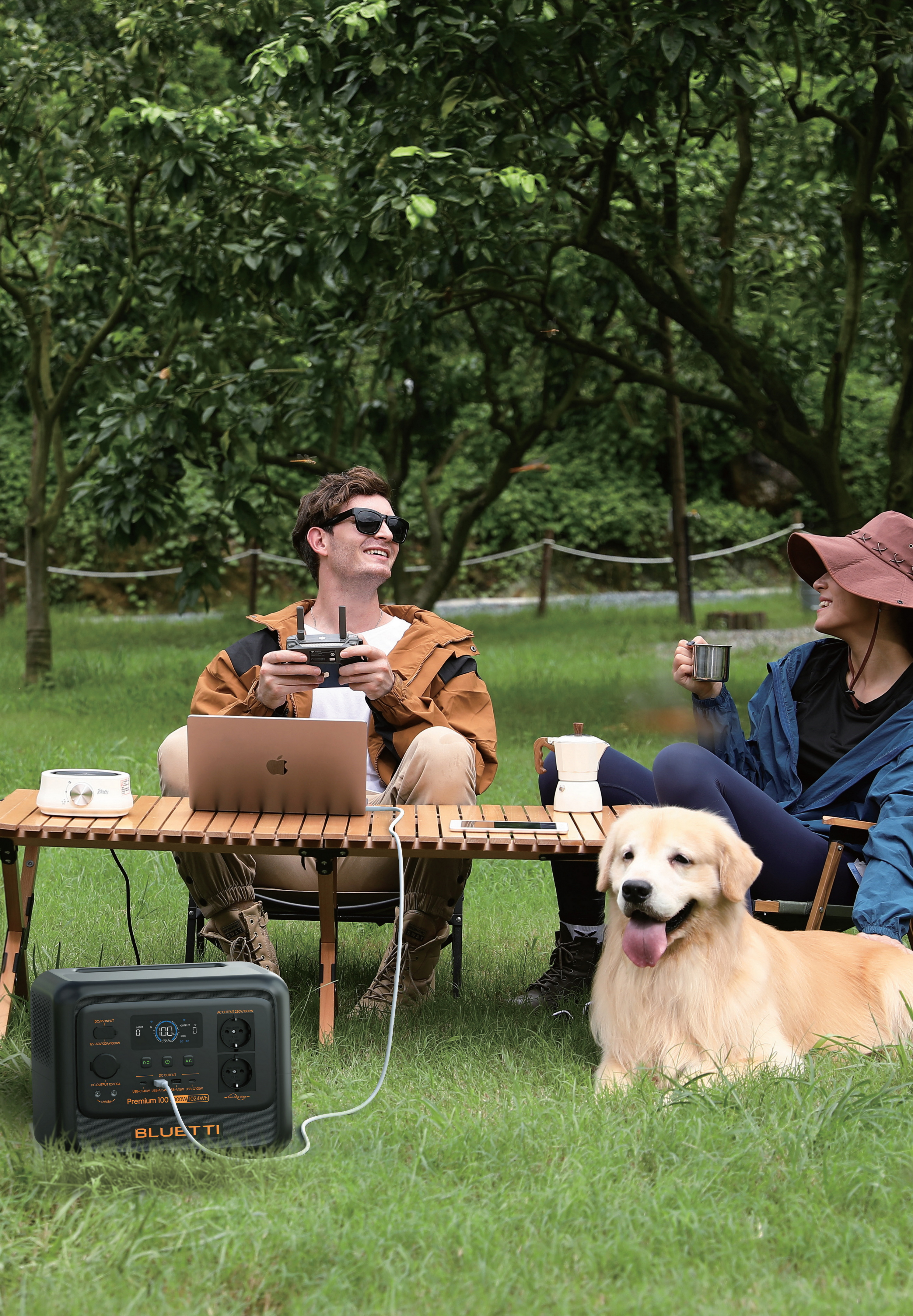 Mężczyzna z pilotem, kobieta z kubkiem, pies leżą na trawie.