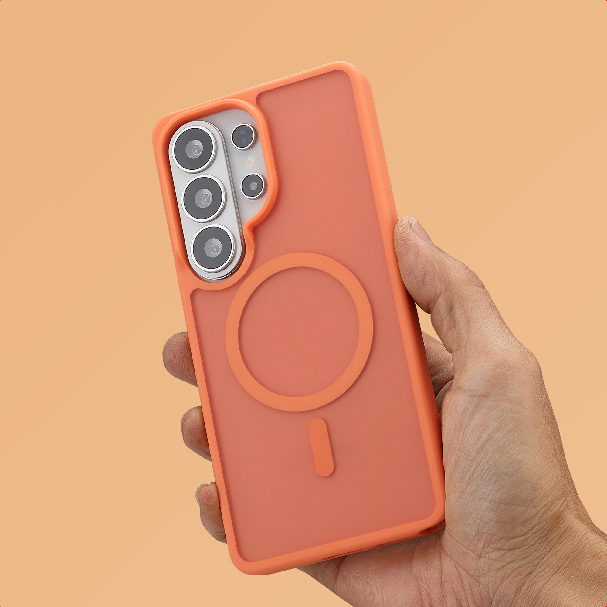 Een hand houdt een koraalkleurige telefoonhoes vast met cameralenzen en een magneetring.