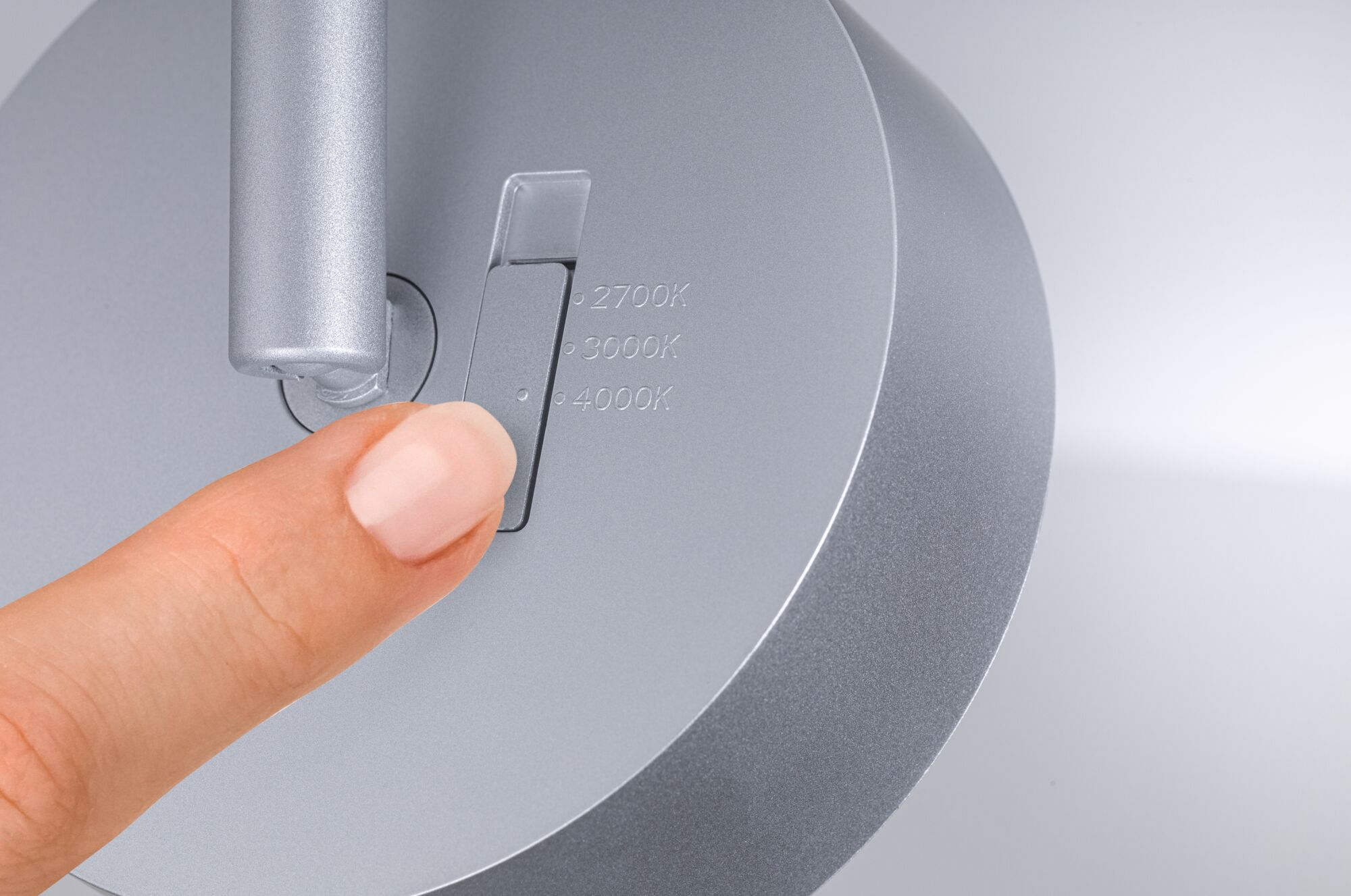 Palec przesuwa przełącznik na srebrnej lampie, aby dostosować temperaturę barwową.