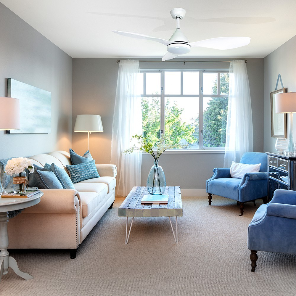Sala de estar con sofá blanco, sillones azules, mesa de centro y ventilador de techo.