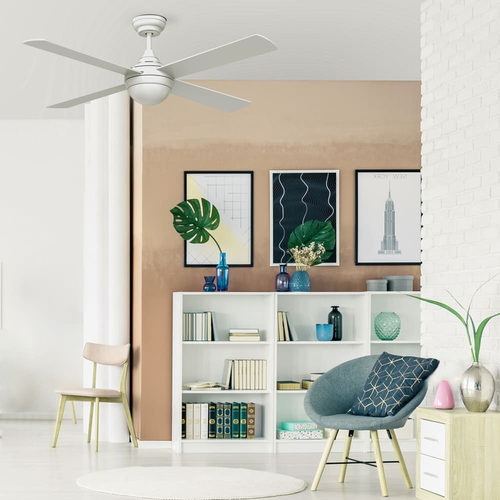 Una sala de estar con ventilador de techo, estantería, silla y cuadros en la pared.