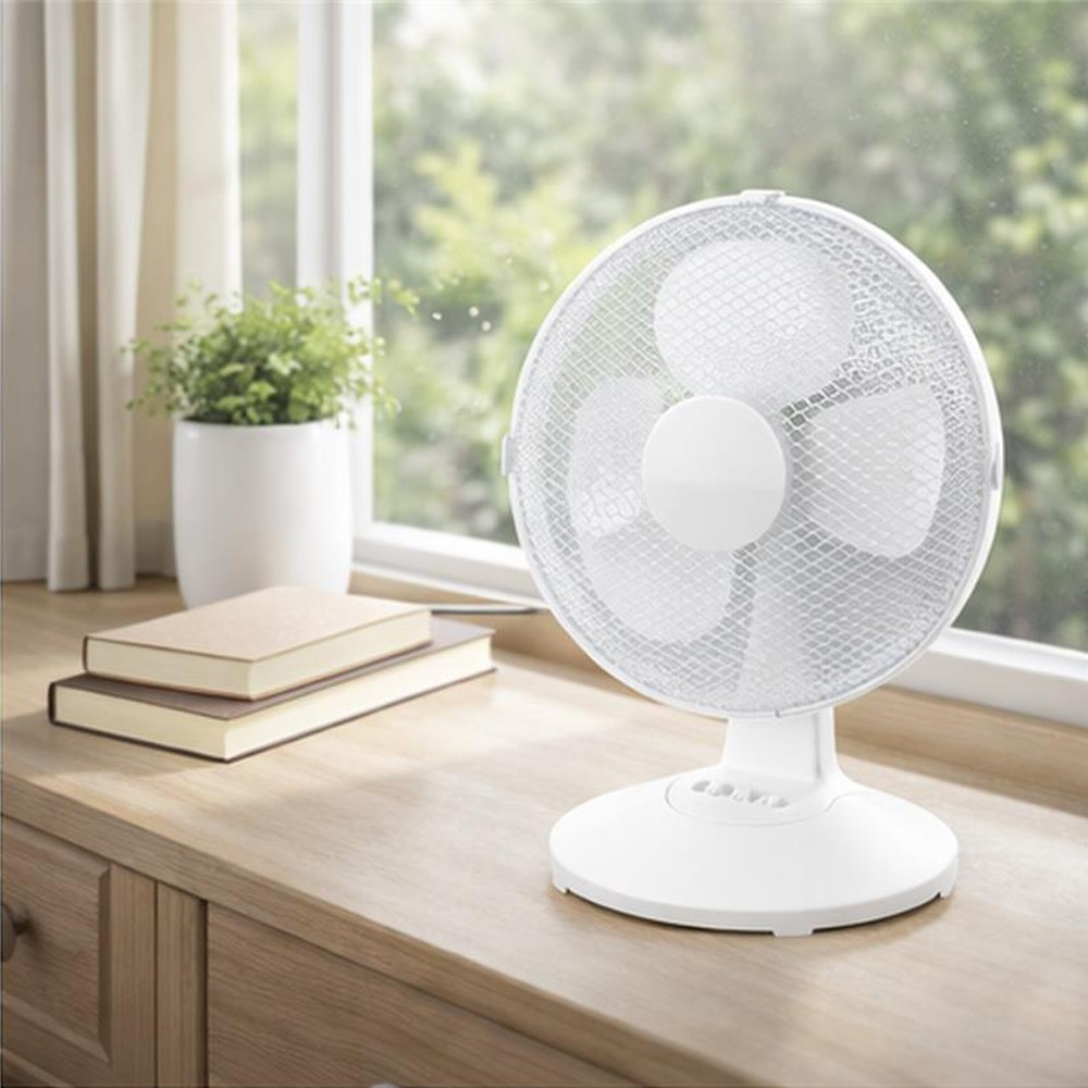 Un ventilador de escritorio blanco está sobre un mueble de madera junto a dos libros y una planta.