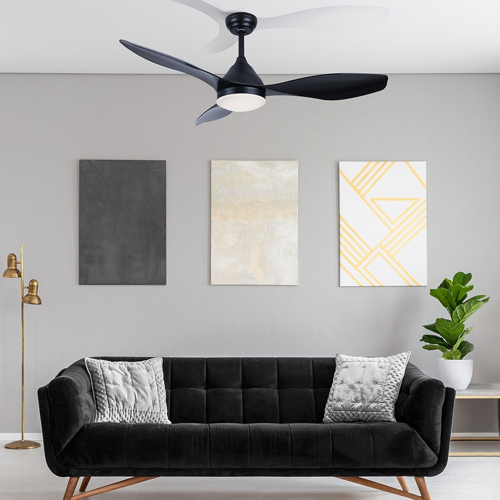Sofá negro con cojines, ventilador de techo, arte en pared y planta.
