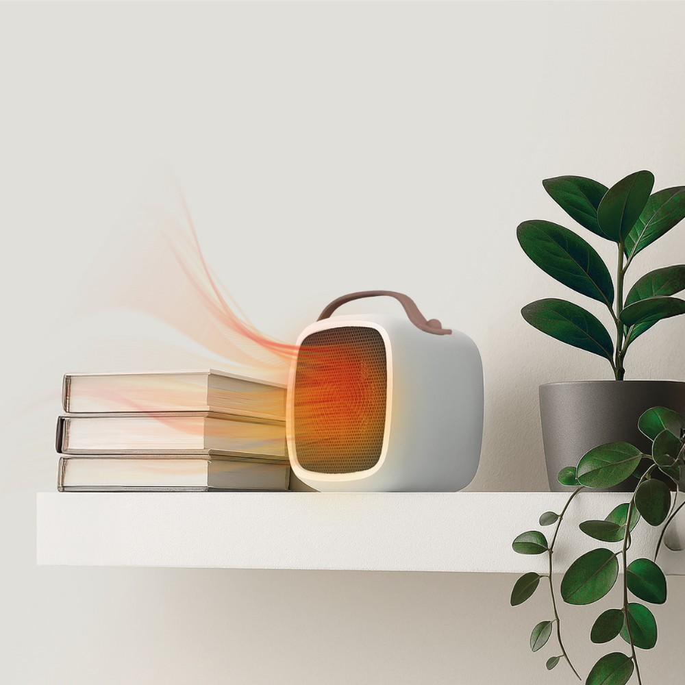 Calentador blanco compacto con asa marrón emitiendo calor. Libros y planta cerca.