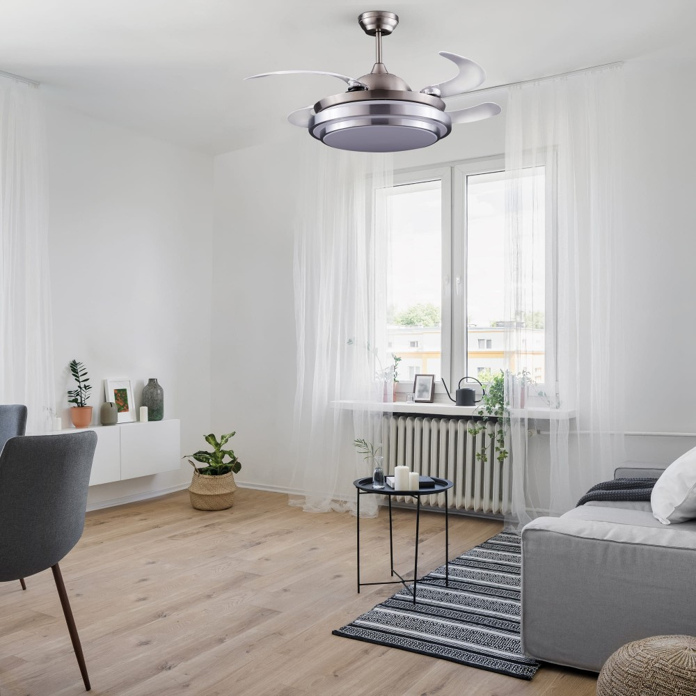 Un ventilador de techo plateado con luz sobre una ventana con cortinas blancas.