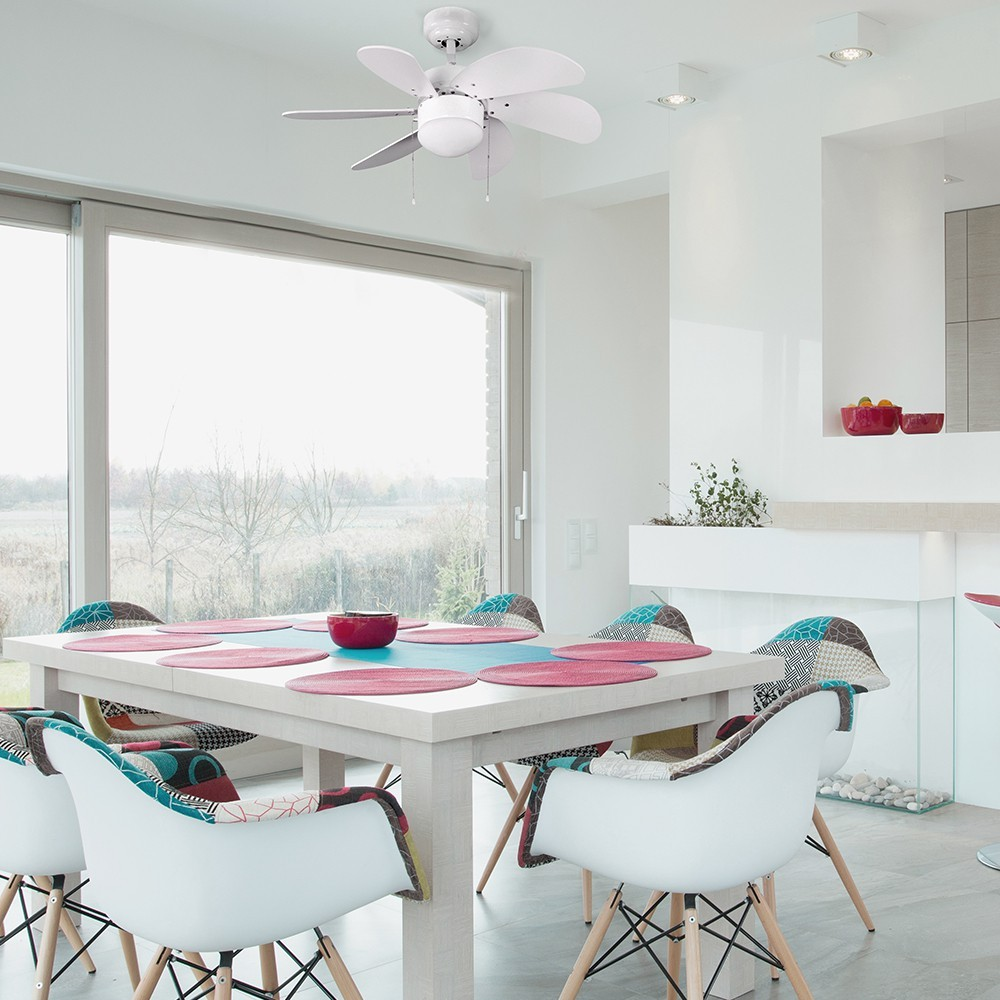 Un ventilador de techo blanco sobre una mesa de comedor con sillas y manteles coloridos.