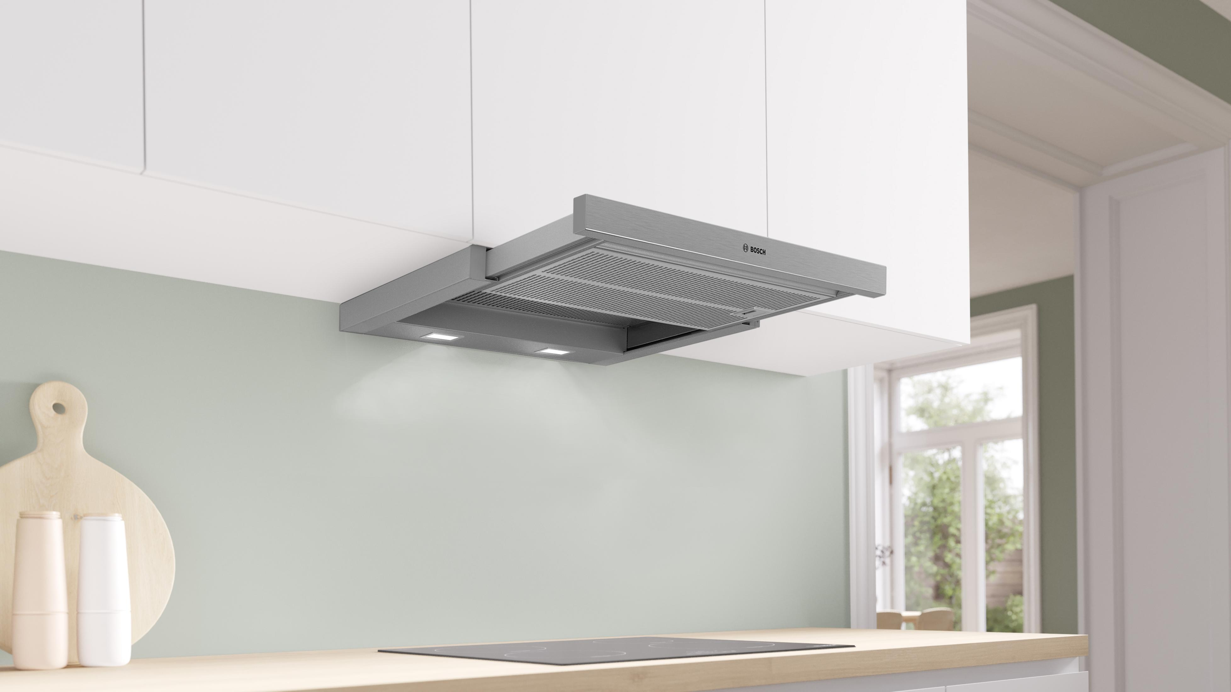 Hotte grise au-dessus de la plaque de cuisson, avec lumières. Armoires blanches au-dessus.