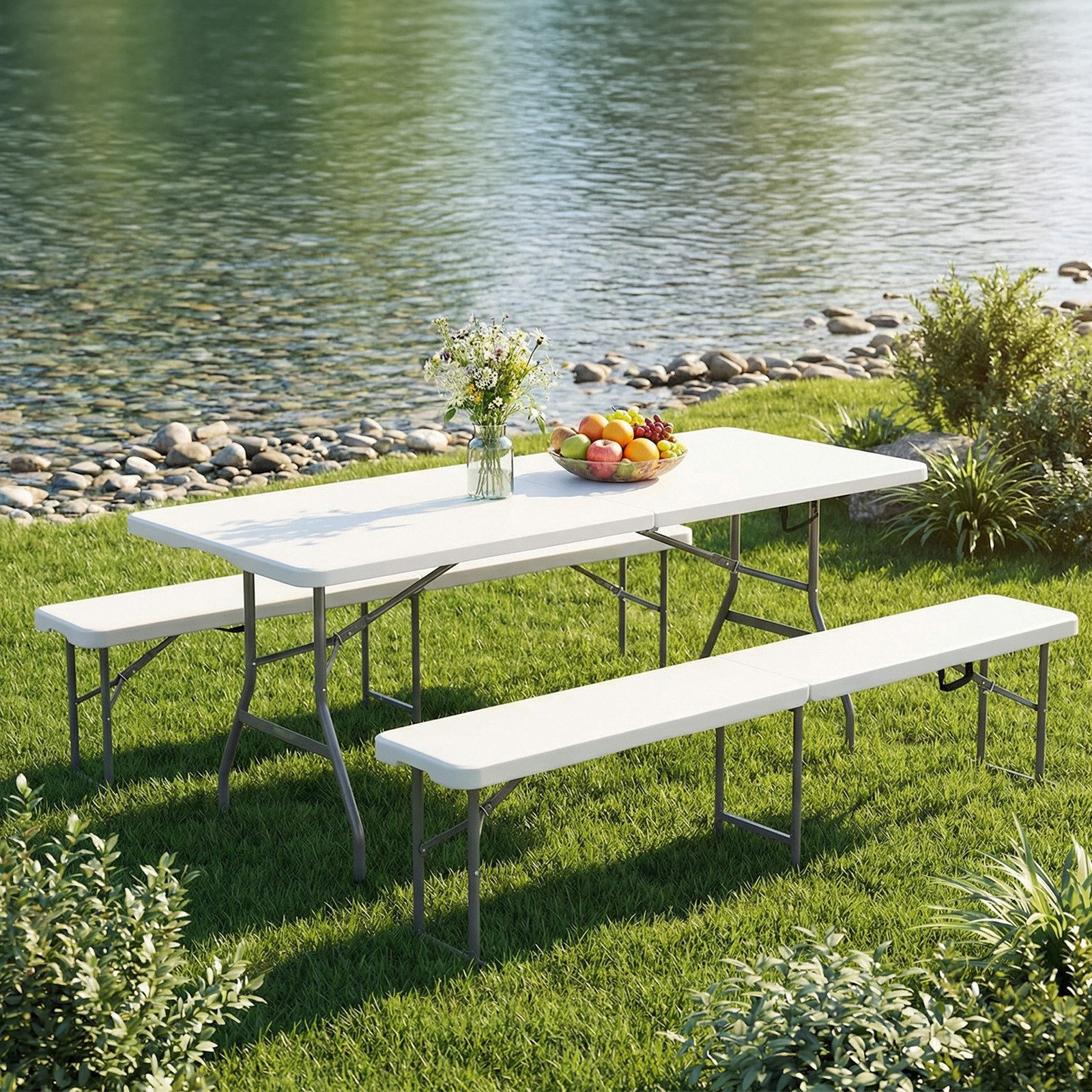Una mesa de picnic blanca con bancos se asienta sobre césped verde junto al agua.