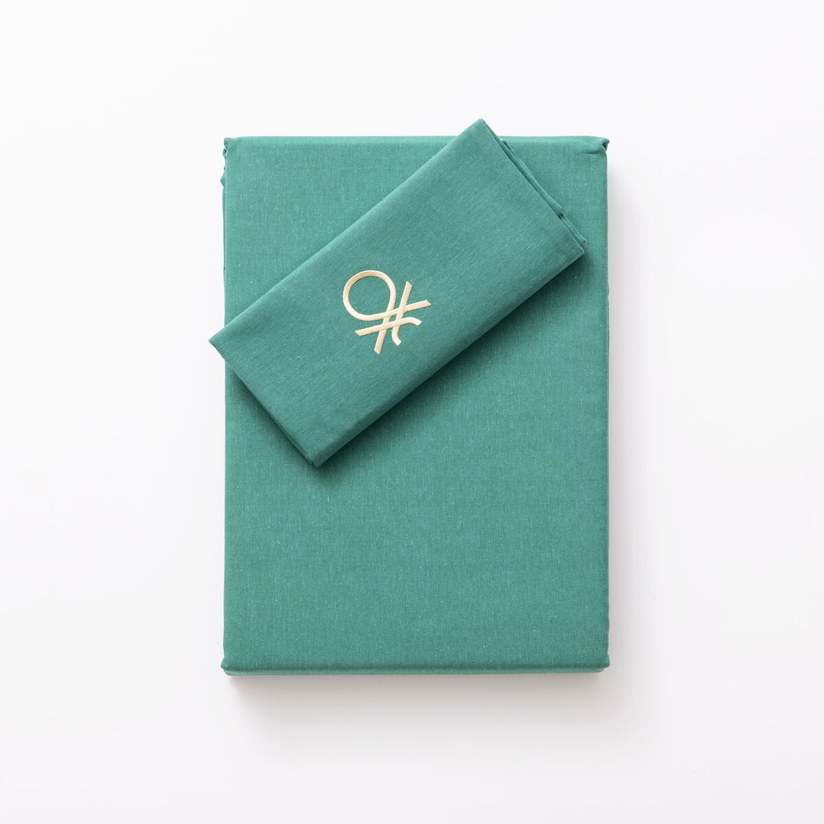 Un libro verde esmeralda con un paño verde esmeralda doblado y un logo dorado encima.