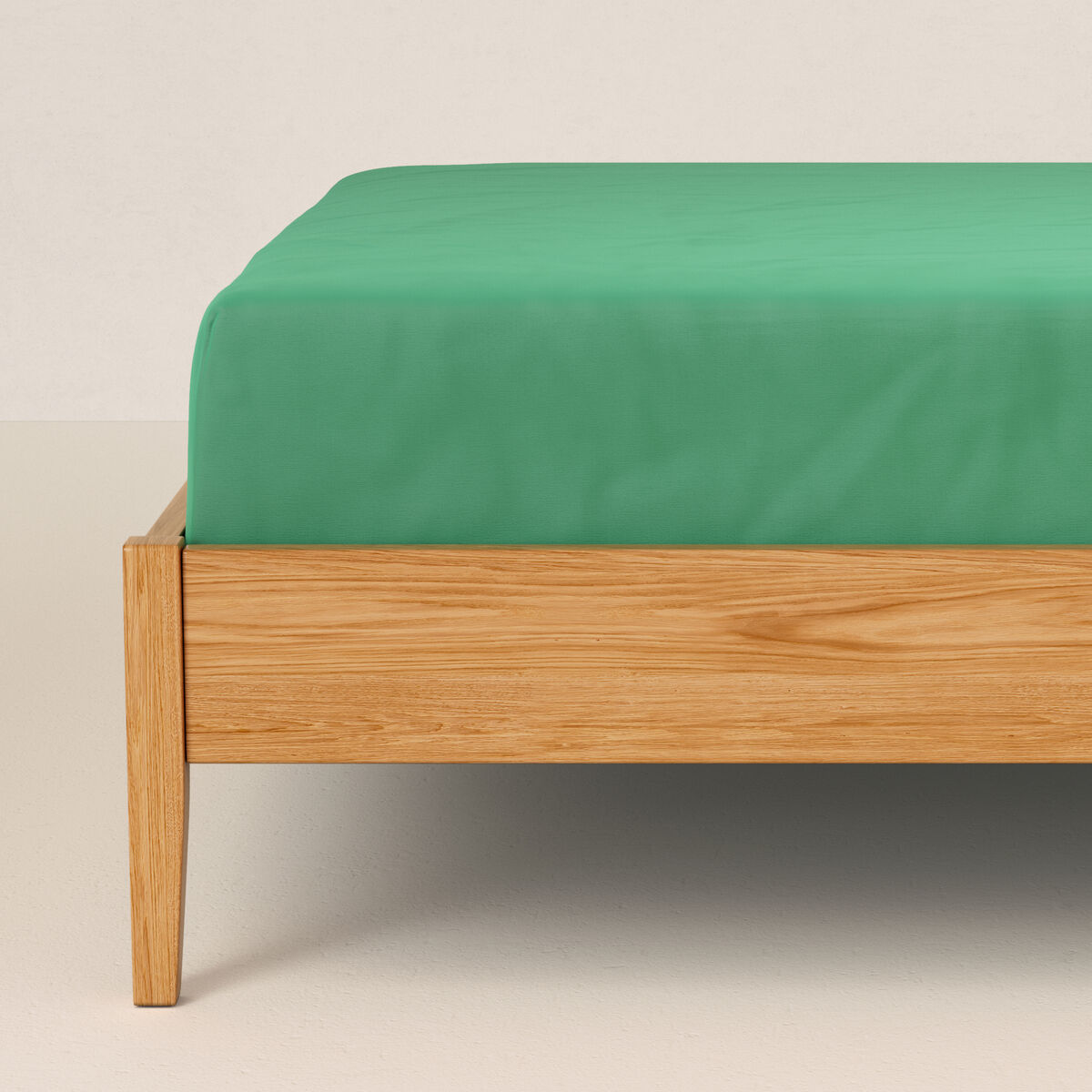 Una sábana bajera verde sobre un somier de madera.