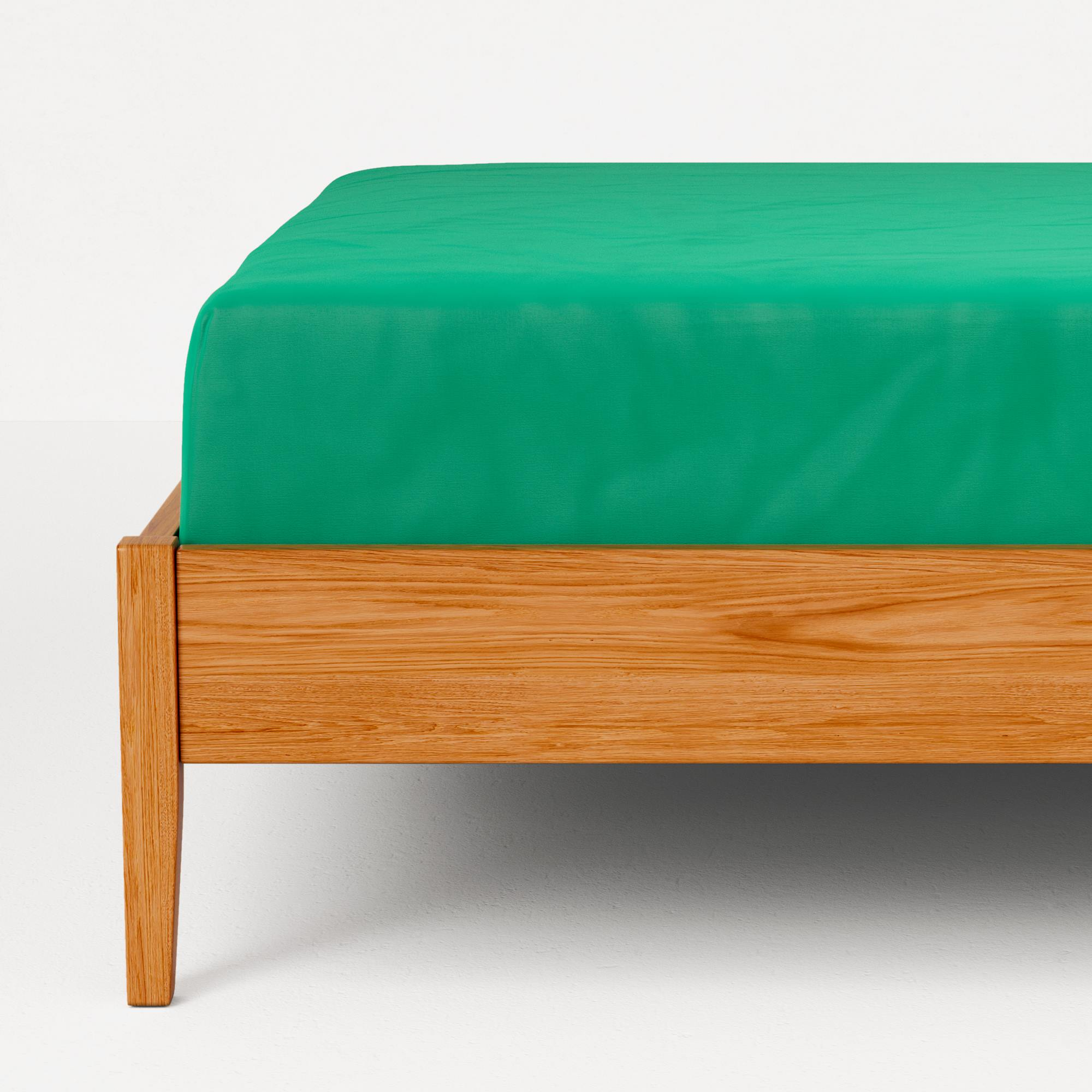 Una sábana bajera verde sobre un somier de madera, vista cercana.