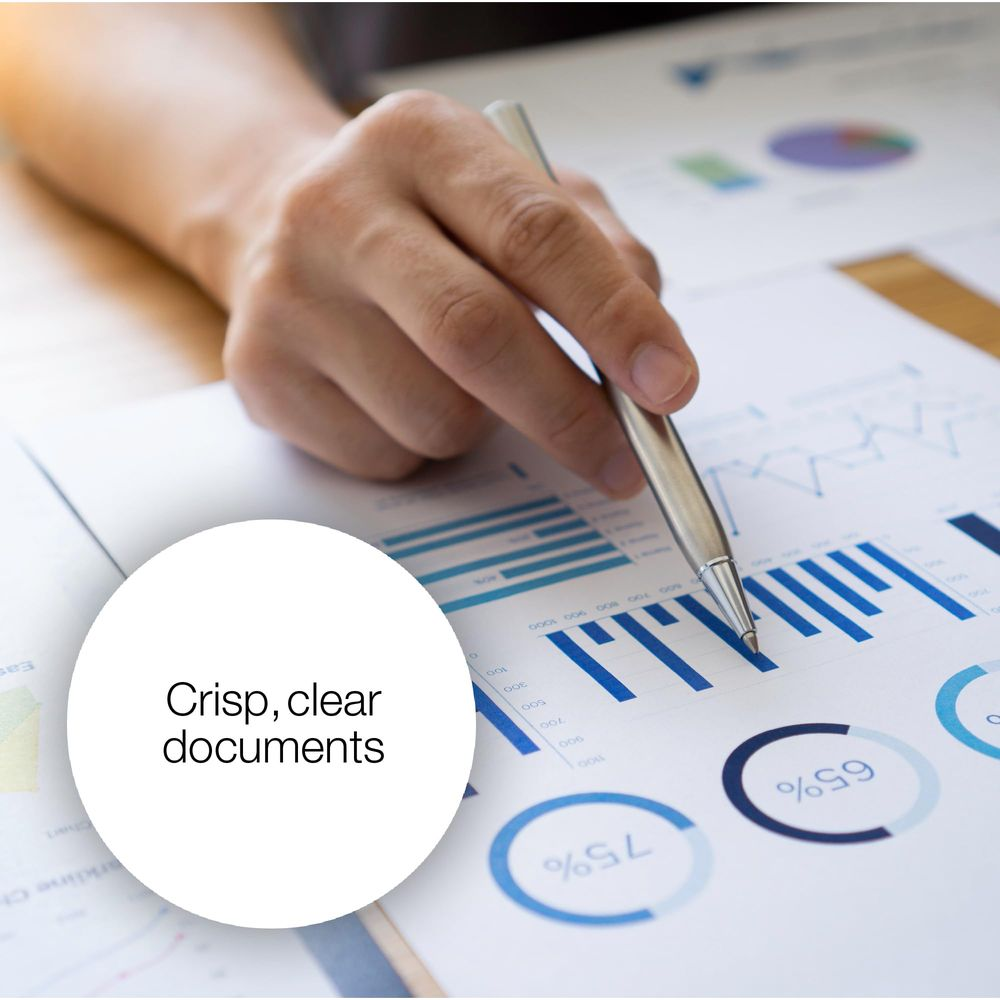 A hand holds a pen over charts and graphs on a desk.