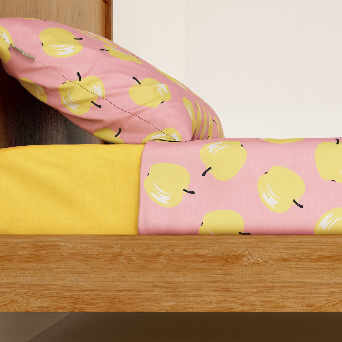 Una almohada rosa con manzanas amarillas y una sábana amarilla en una cama de madera.