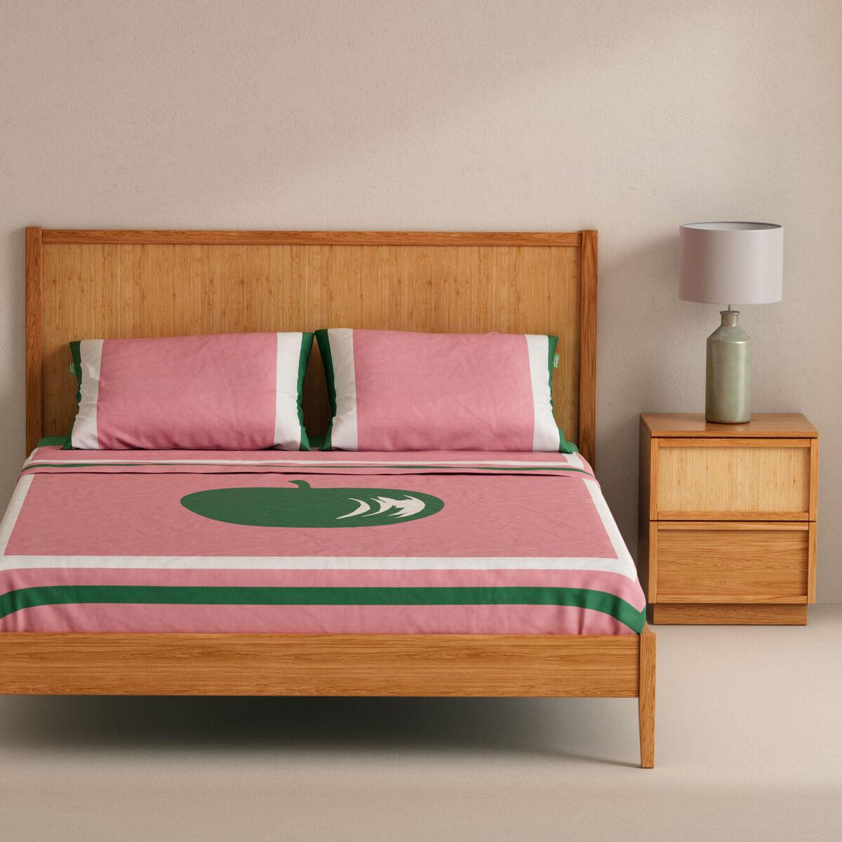 Una cama de madera con ropa de cama rosa con manzanas verdes y rayas.