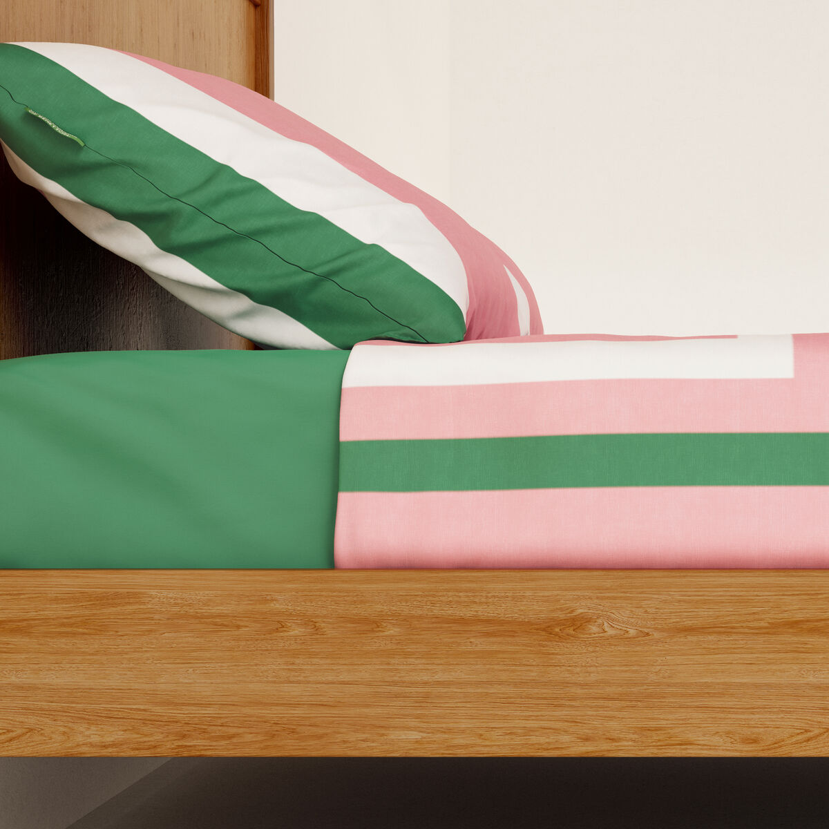 Una almohada a rayas descansa sobre una cama con rayas verdes y rosas.