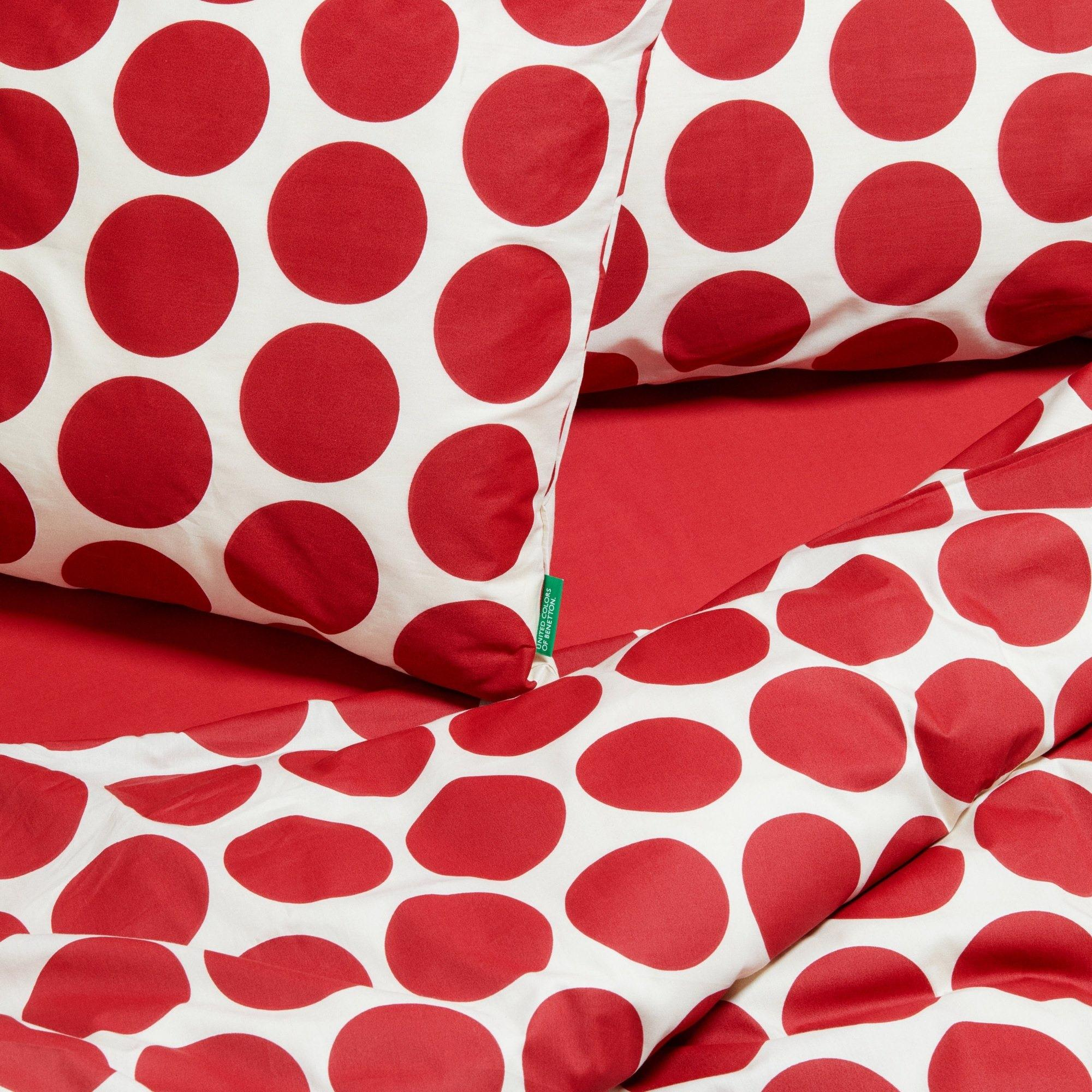 Ropa de cama blanca con grandes lunares rojos y una sábana roja.