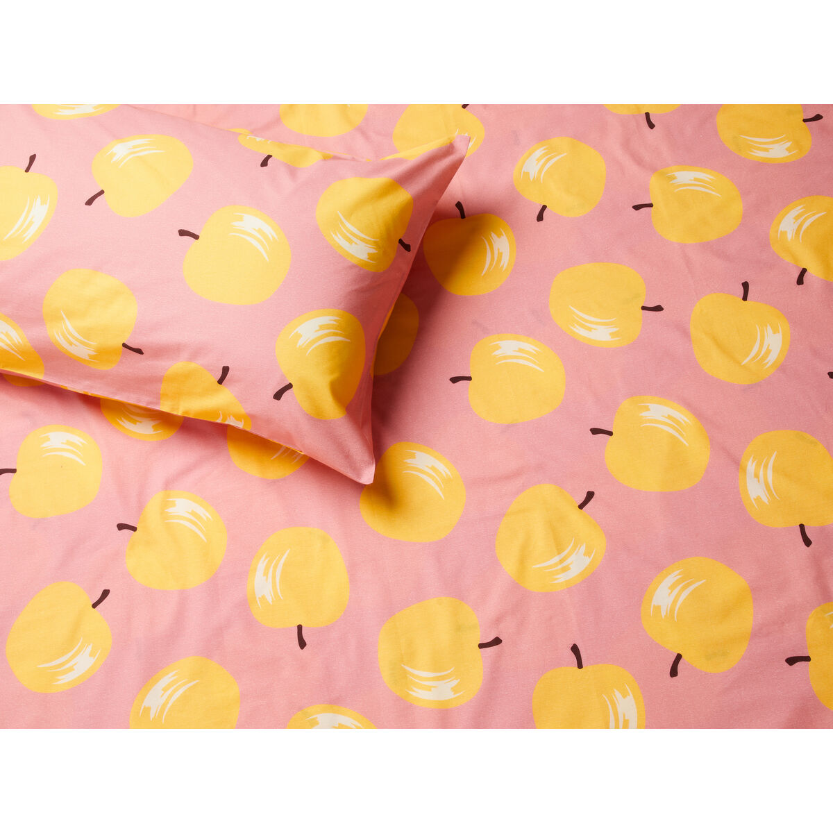 Una funda de almohada y ropa de cama con manzanas amarillas sobre fondo rosa.