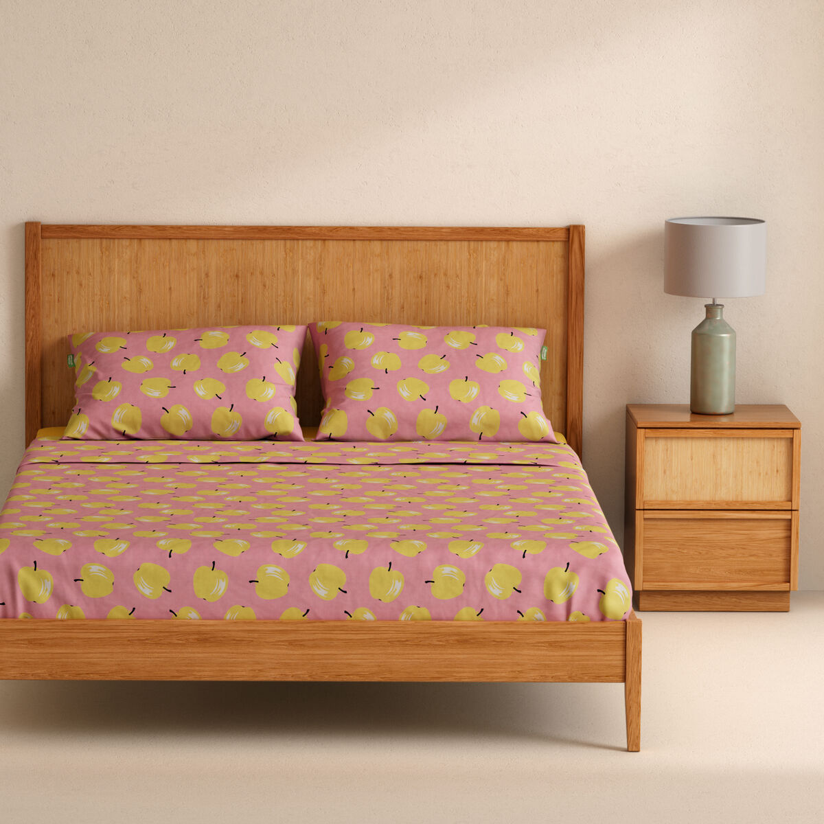 Una cama de madera con ropa de cama rosa con manzanas amarillas y dos almohadas.
