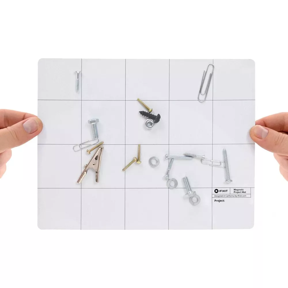 Ręce trzymają magnetyczną matę ze śrubami, nakrętkami i spinaczami.